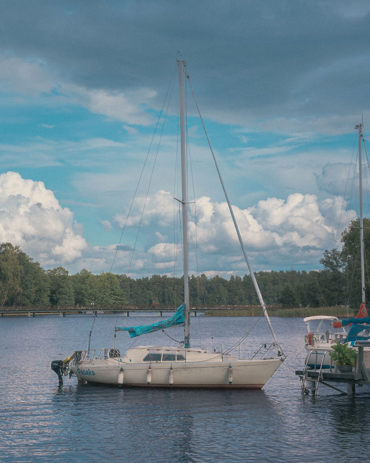 Several sailboats moored in a tranquil lake with trees lining the shore under cloudy skies.