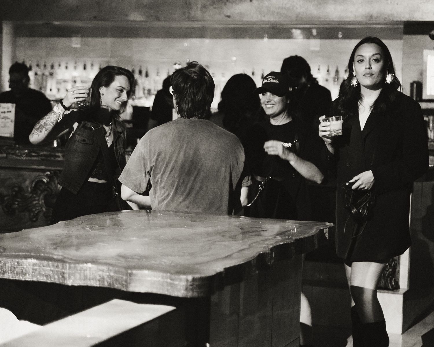 Long bar counter with patrons seated in moody black and white lighting.