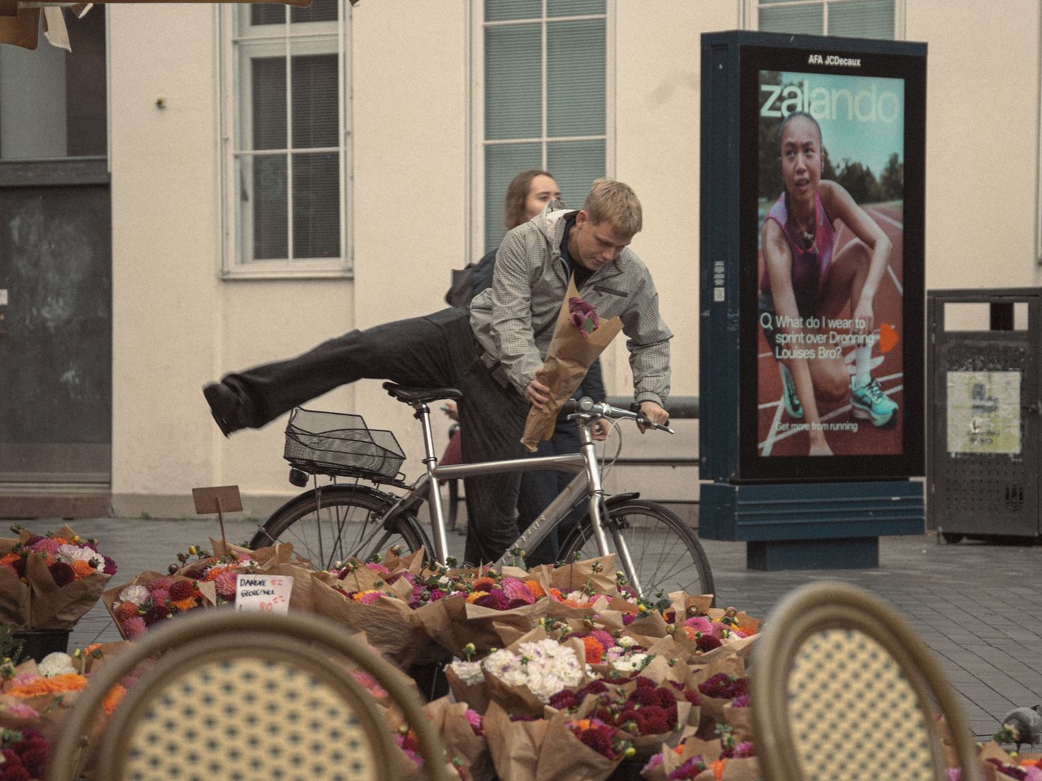 Street scene with cafe chairs and decorative floral arrangements outside a building.
