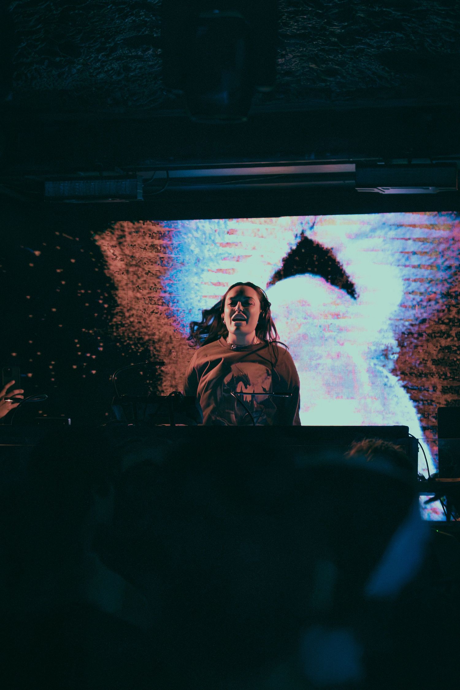 Dark atmospheric concert photo showing silhouetted figures performing on stage with moody blue lighting.