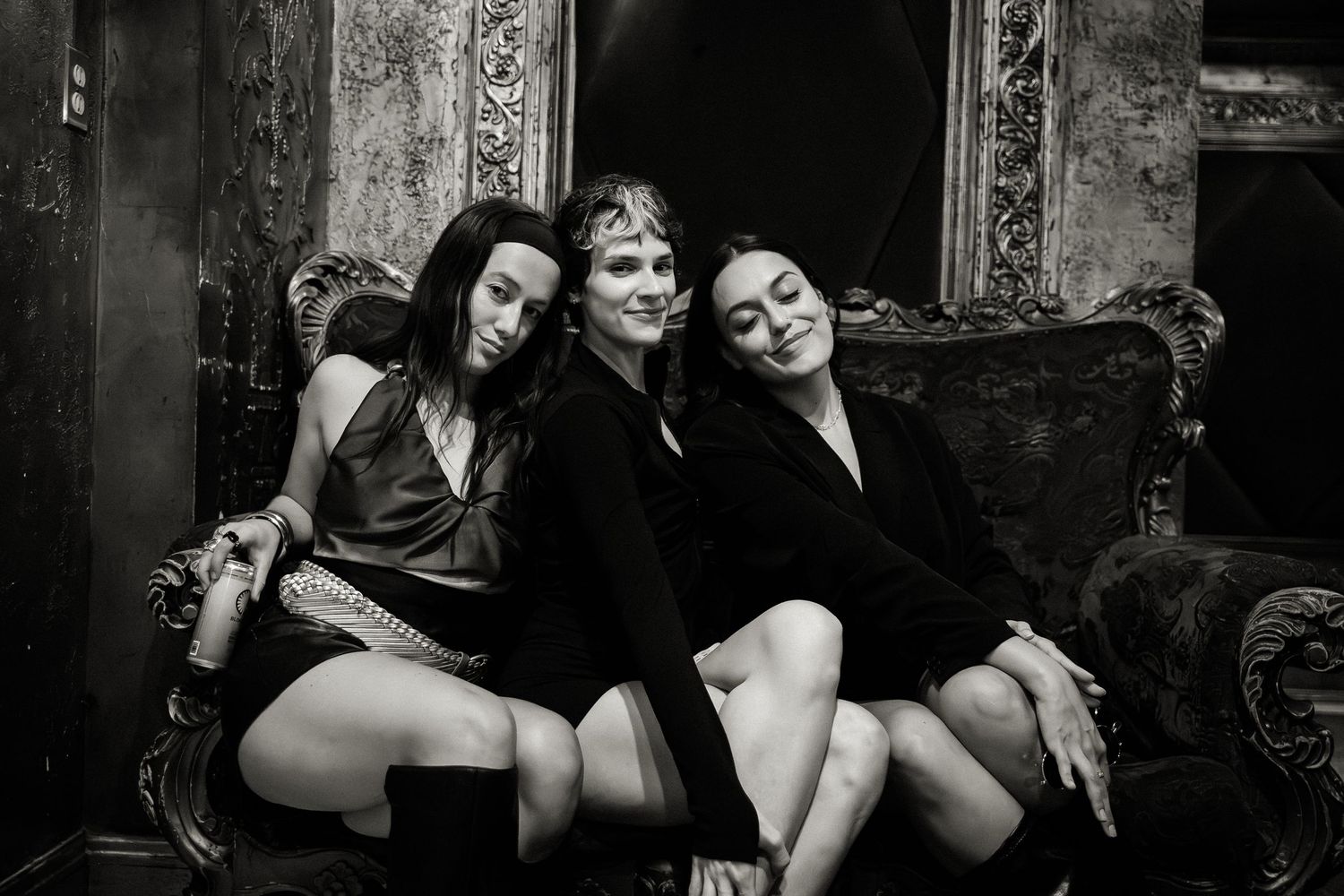 Black and white portrait of people lounging on vintage furniture in an artistic setting.