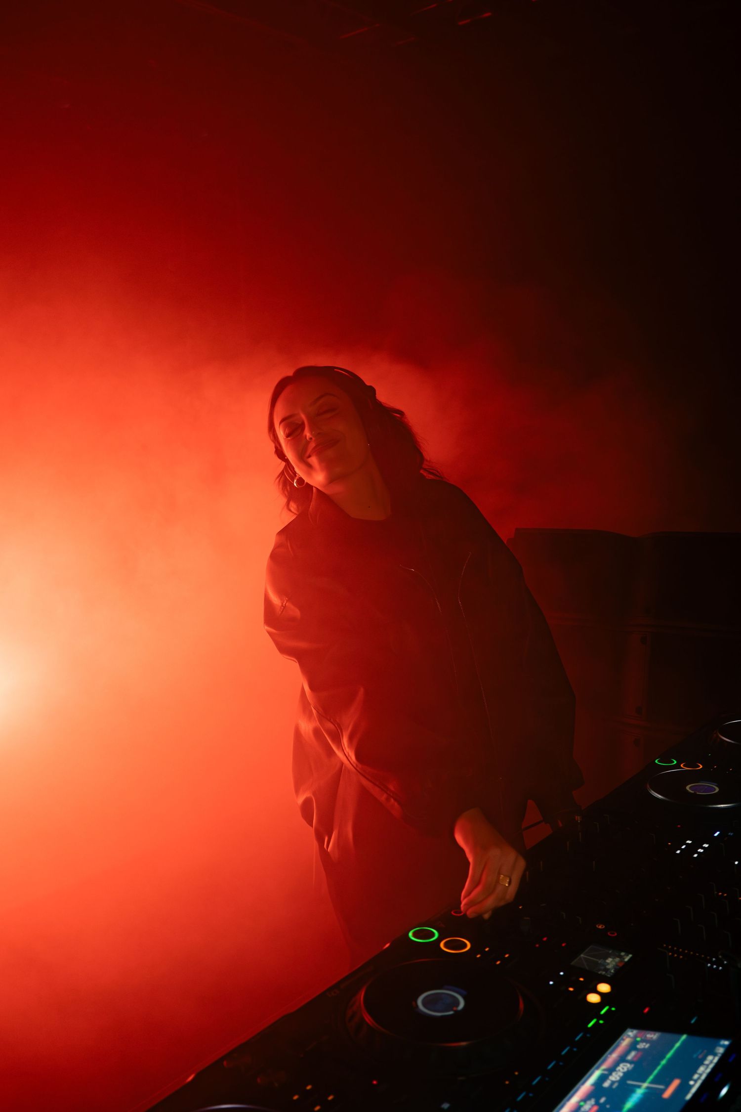 A DJ performs at a nightclub under dramatic red lighting while working the mixer deck during a performance.