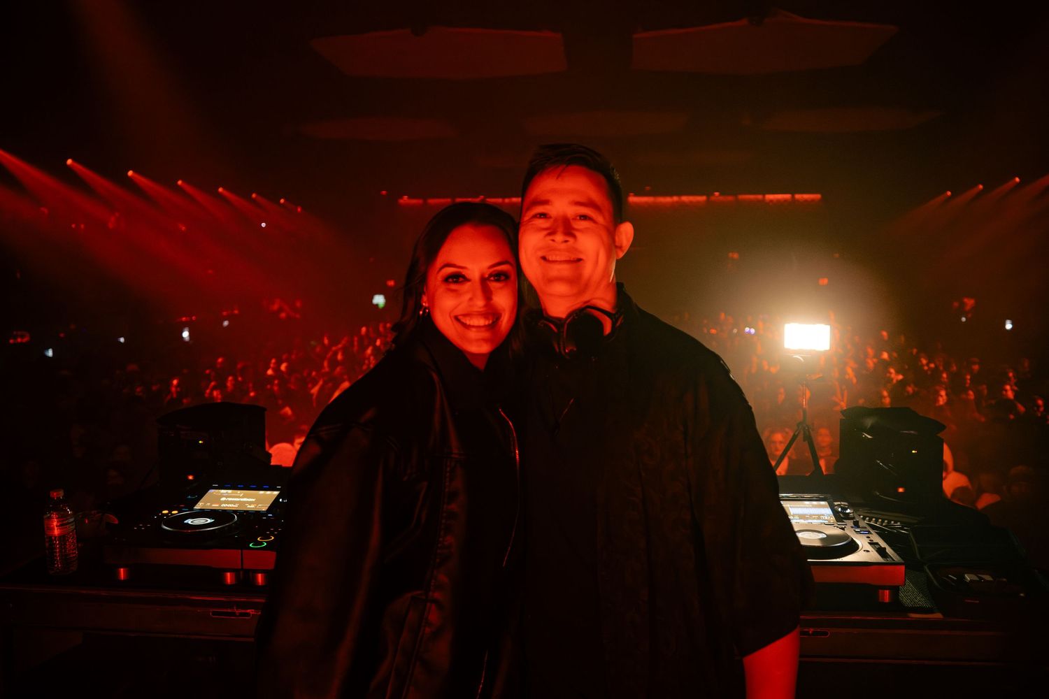 Concert crowd enjoying a live performance in a dark venue with red lighting and stage effects.