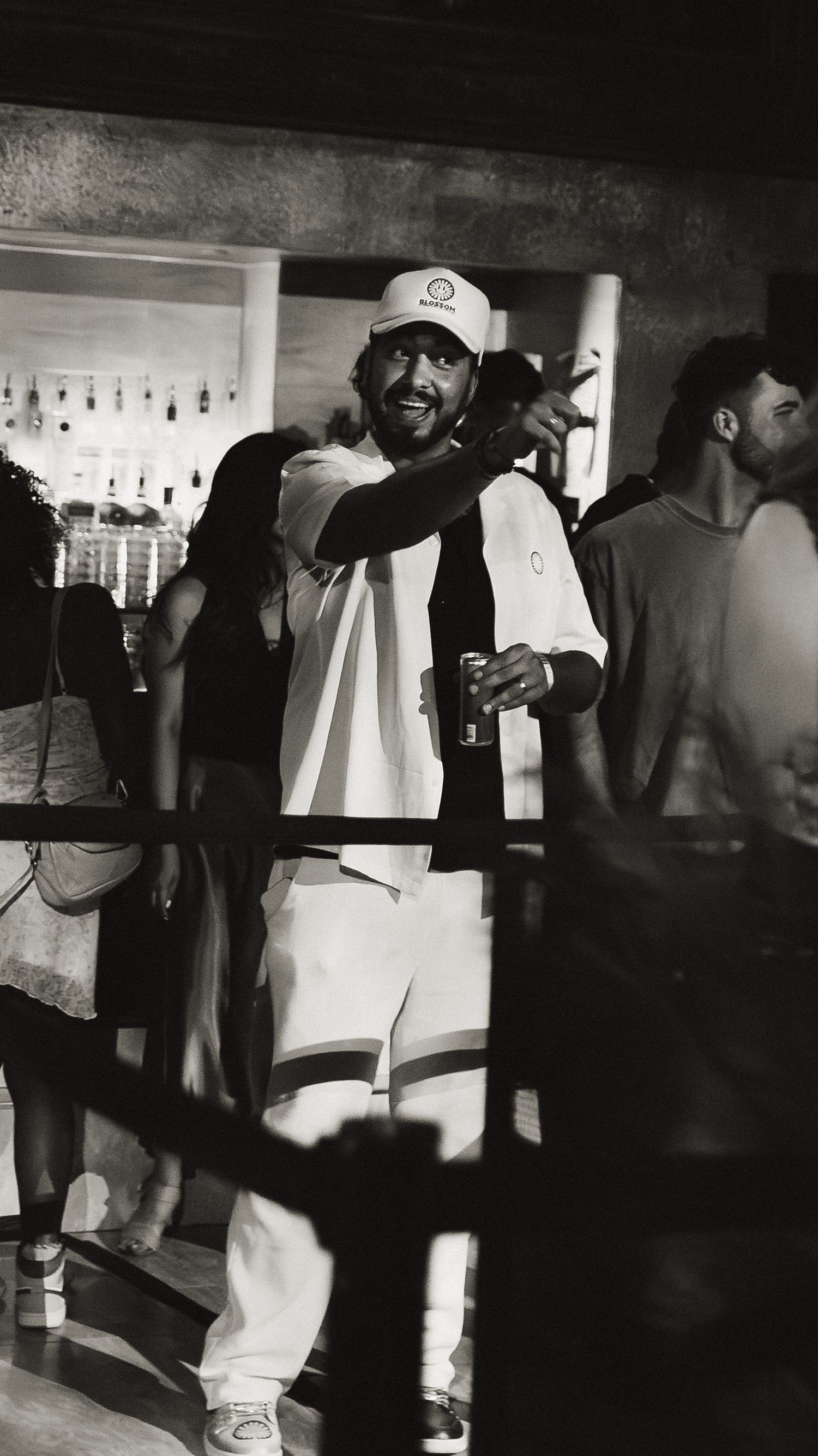 Person in white outfit and baseball cap enjoying themselves at a crowded bar.