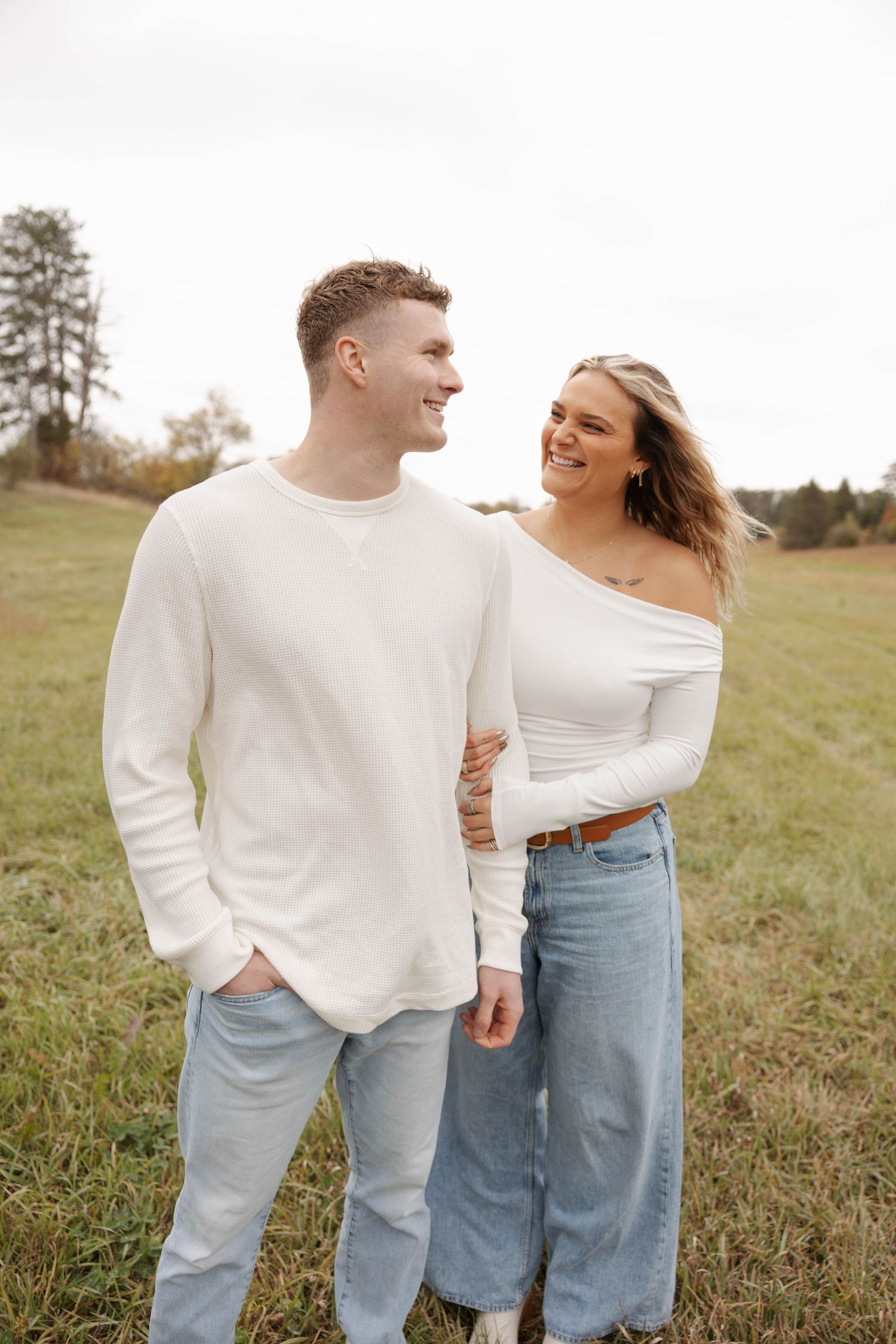 Couple in white sweaters sharing candid moment in grassy field.