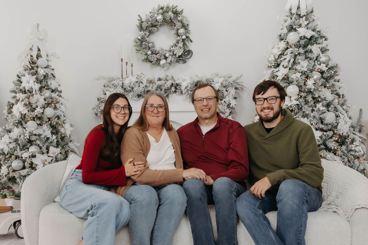 Group sits together on white couch surrounded by snow-covered Christmas trees.