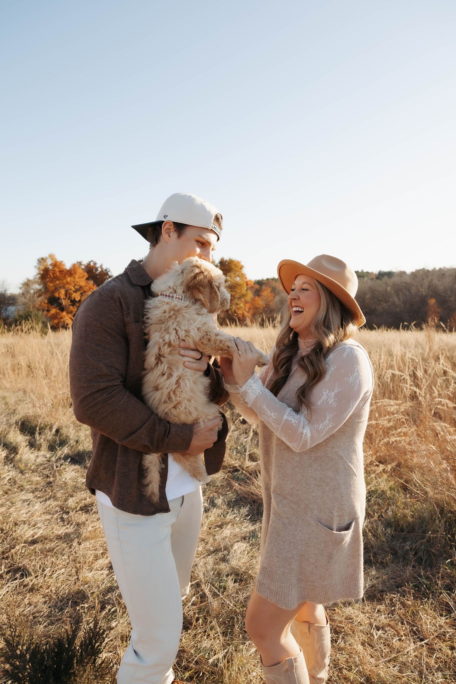 Couple playing with their fluffy dog in a sunlit autumn field.