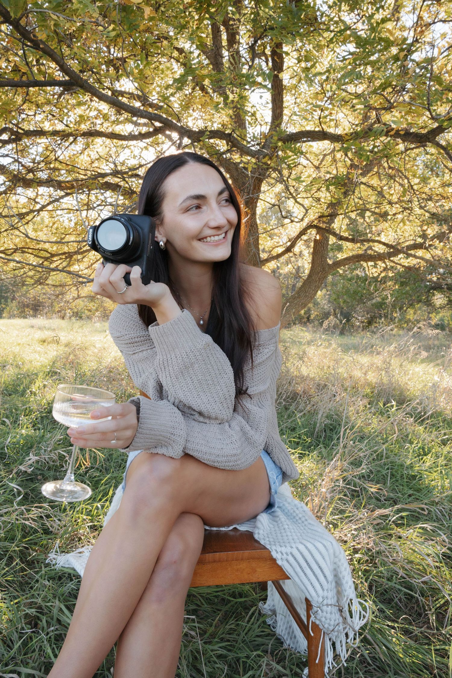 A photographer in a cozy sweater enjoys wine and takes photos in a sunlit autumn field.