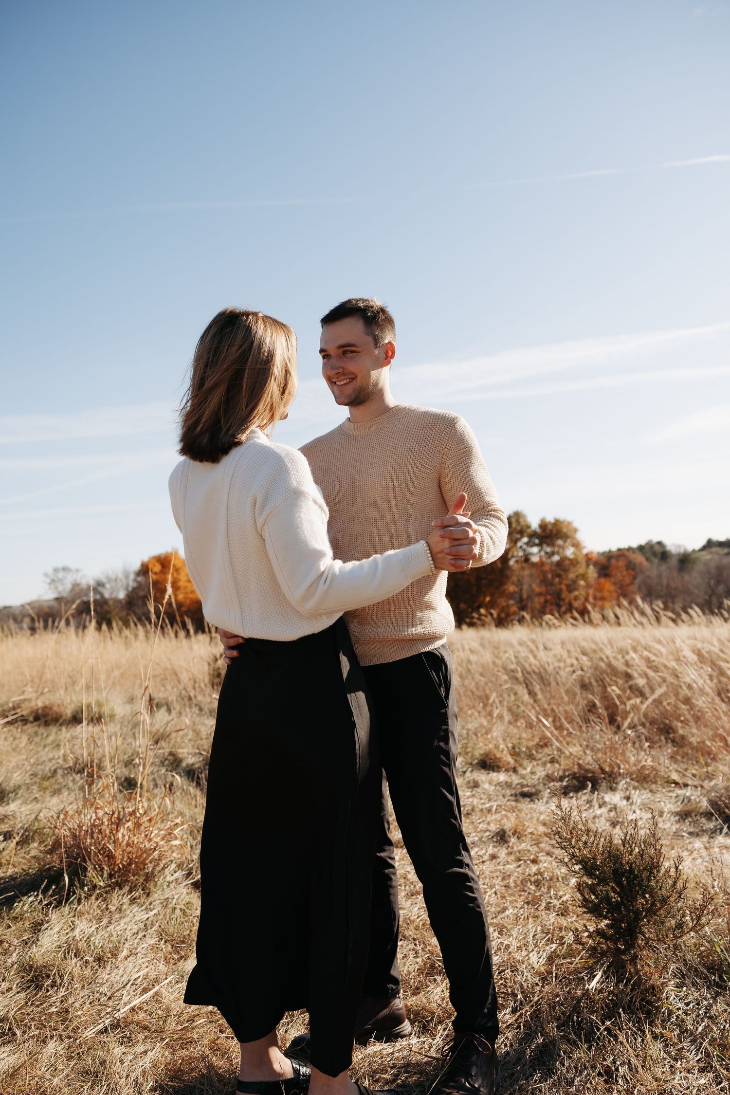 A couple shares a tender moment in a golden autumn field at sunset.
