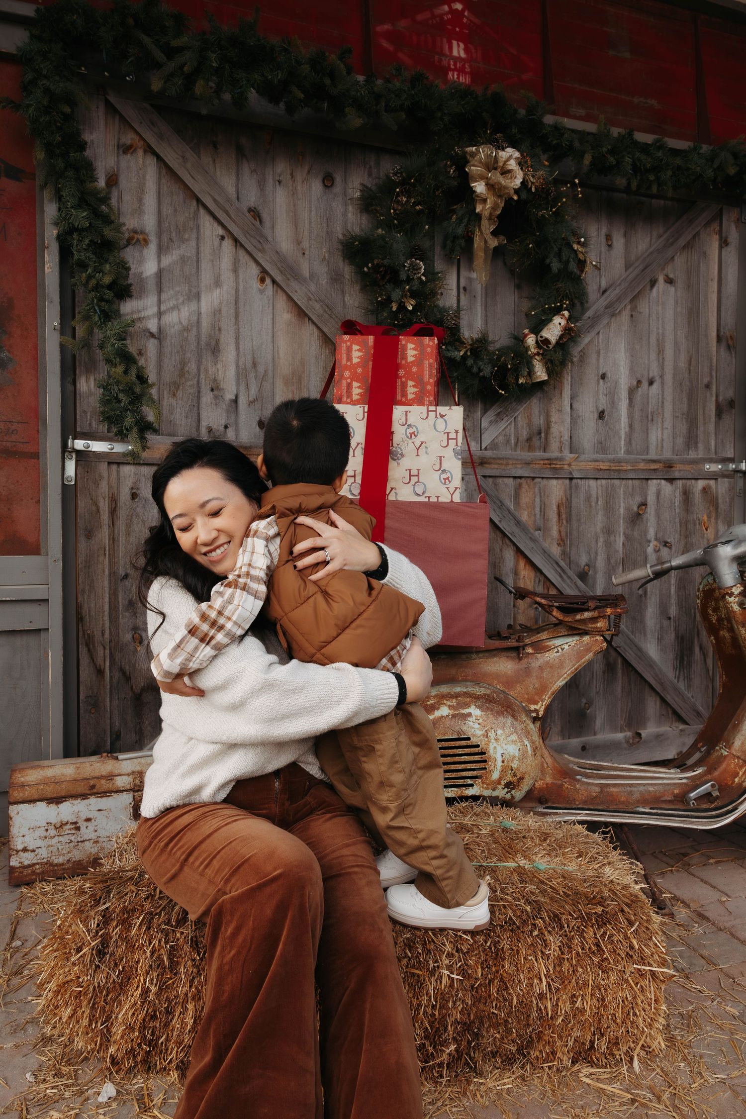 Parent and child share tender moment on hay bale with festive decorations and vintage decor.