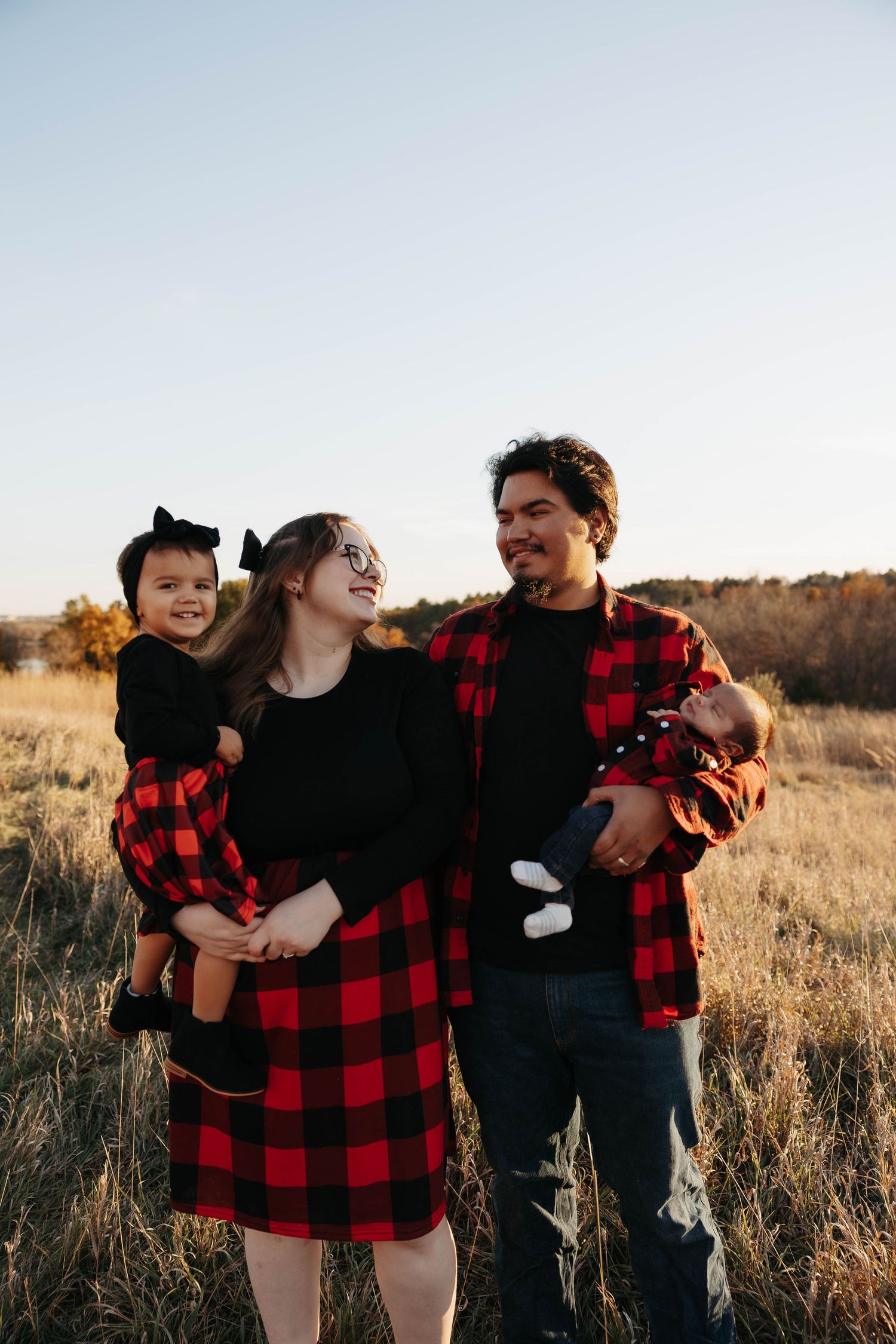 Family wearing matching buffalo plaid outfits poses in autumn field.