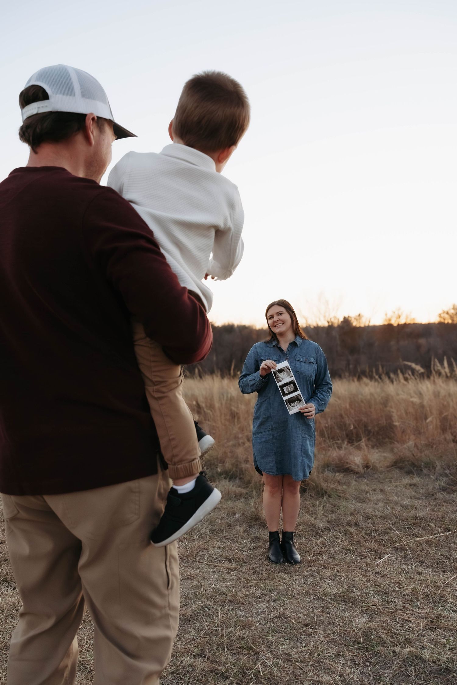 Family members reacting joyfully to ultrasound photos in a field.