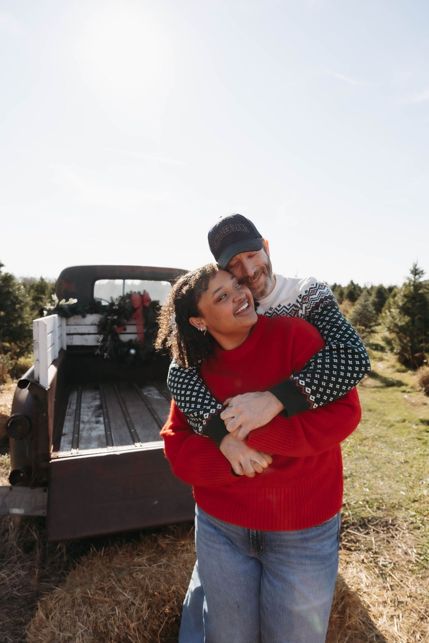 Couple embraces playfully in front of vintage truck during outdoor photoshoot.