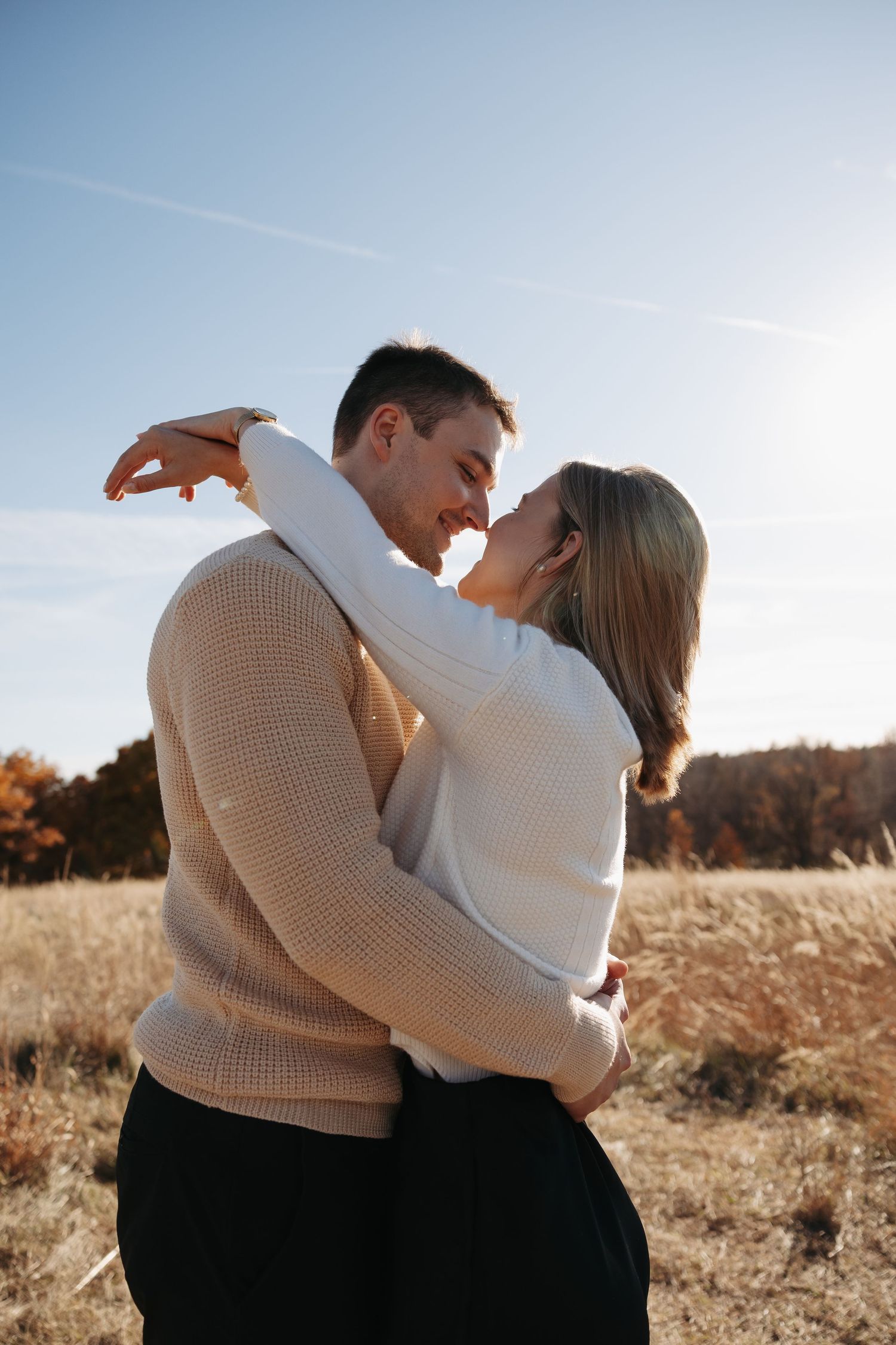 Couple in neutral sweaters embracing in a sun-drenched autumn field.