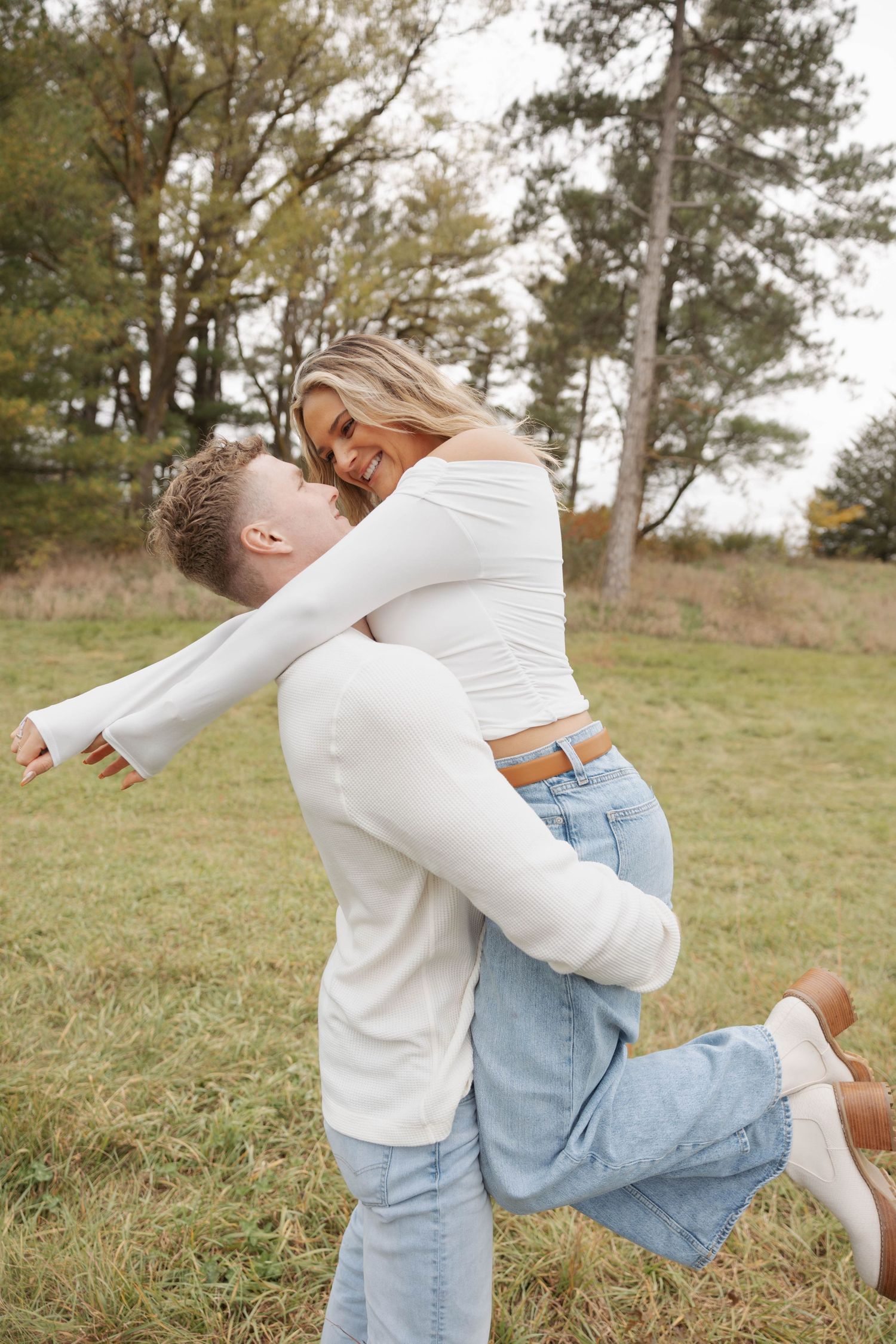 Playful couple in white and denim spins and dances in grassy field.