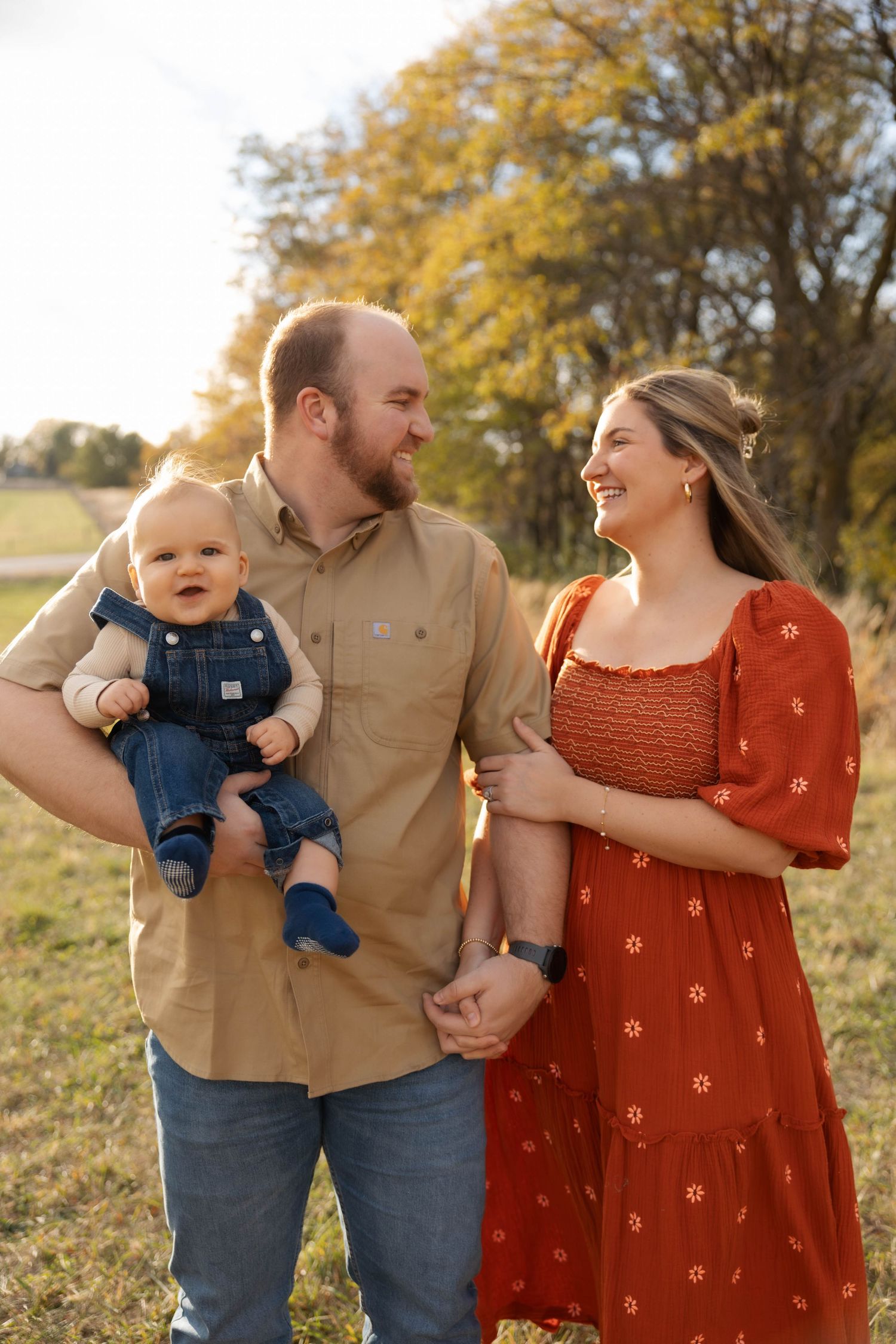 A family in coordinating fall outfits poses together in a golden field at sunset.