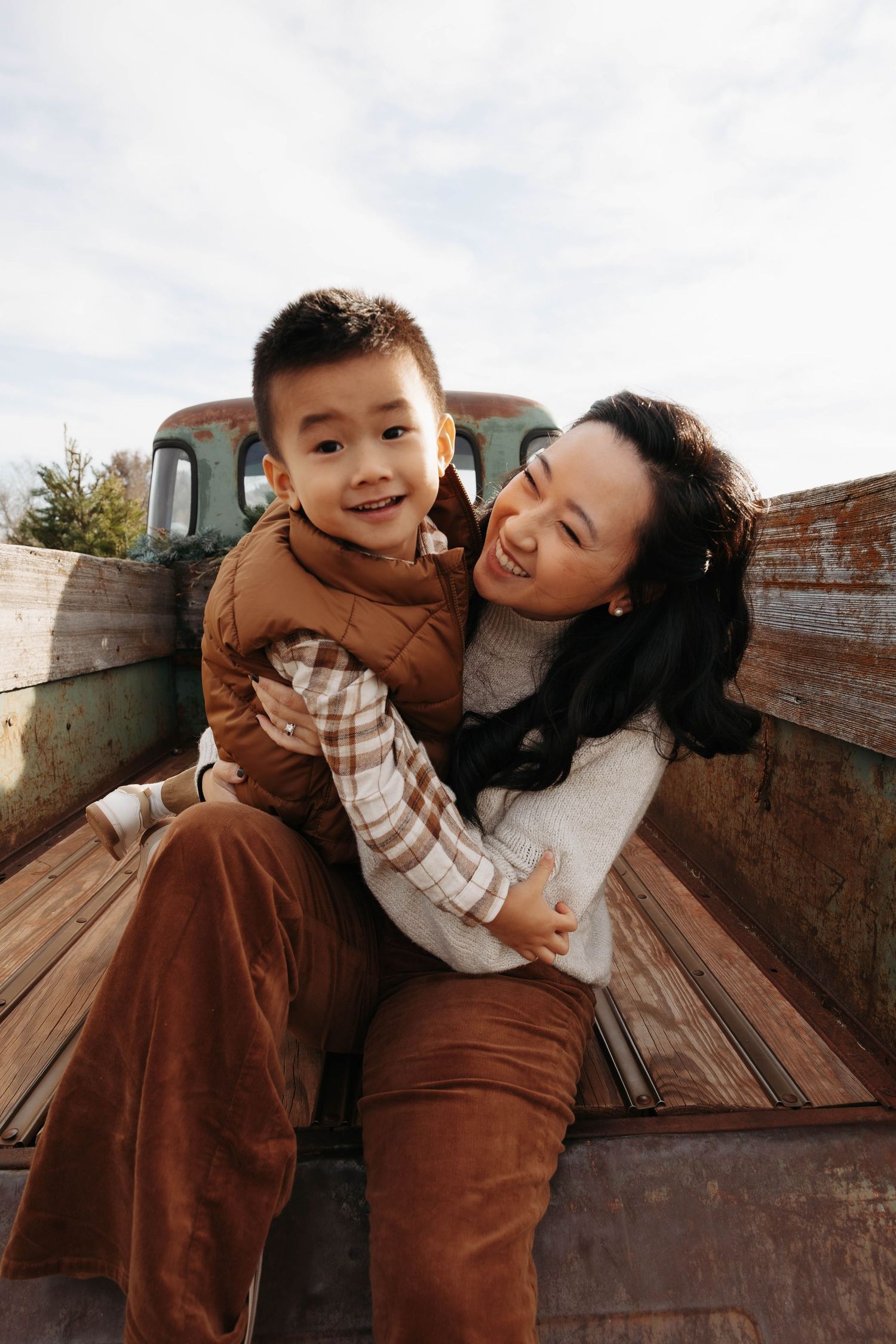Parent and child share joyful moment in back of vintage truck during outdoor photoshoot.