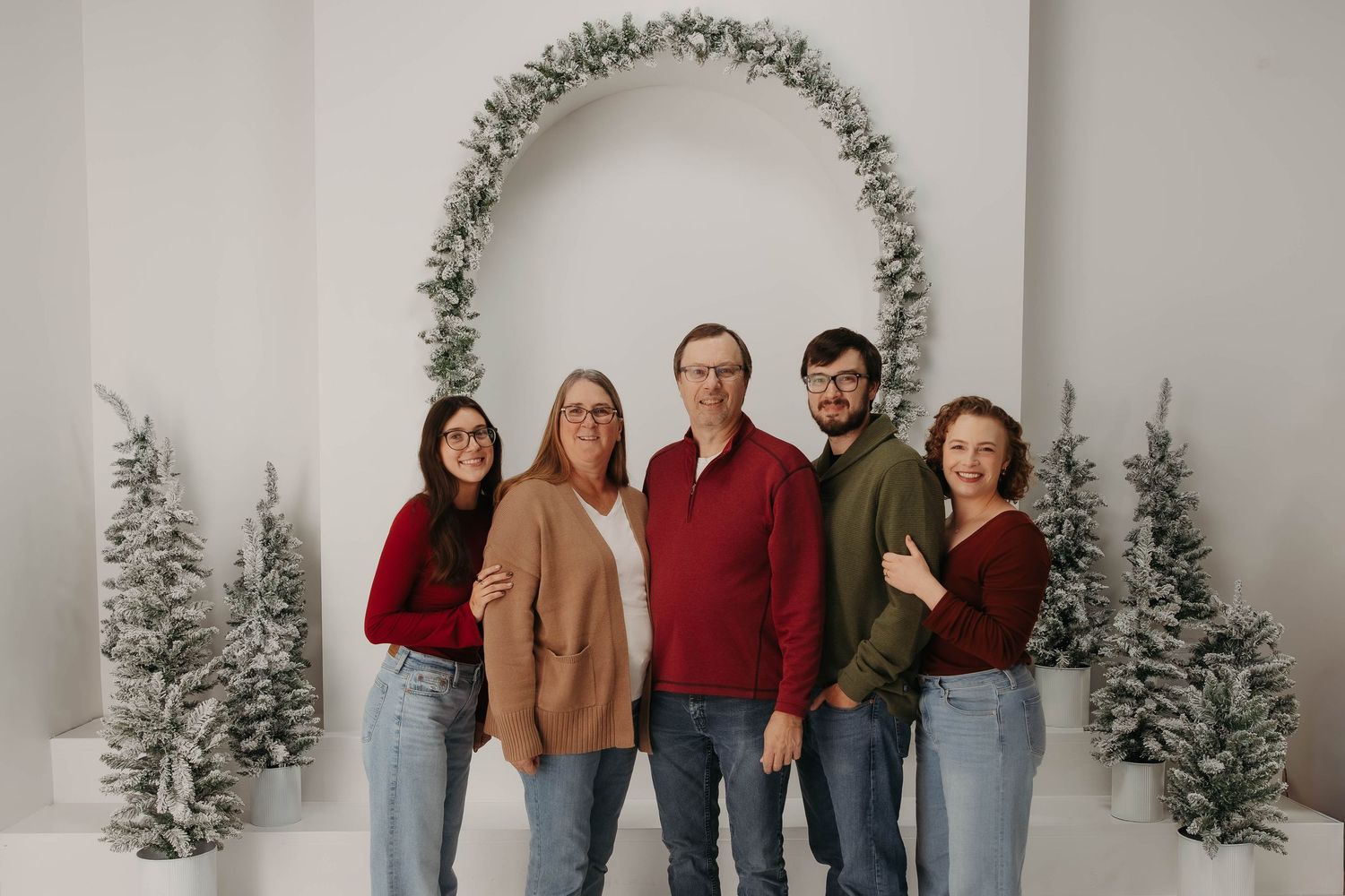 Group poses in front of winter-themed arch with flocked trees and holiday decor.