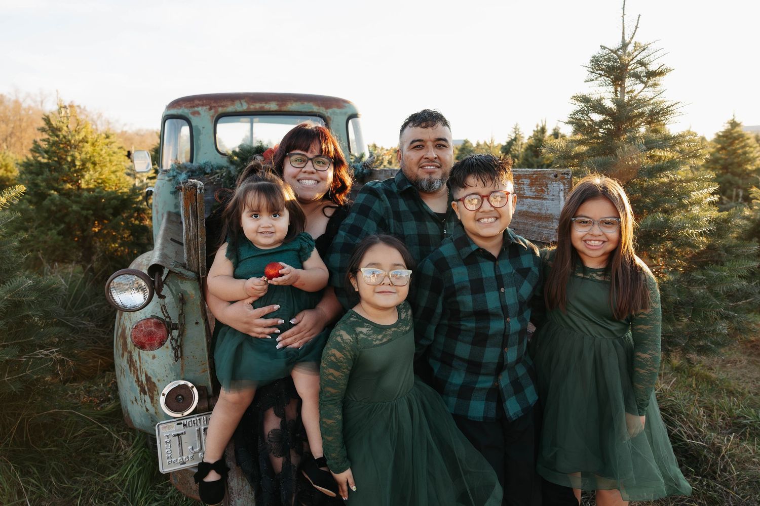 Family poses together in front of vintage truck at Christmas tree farm.