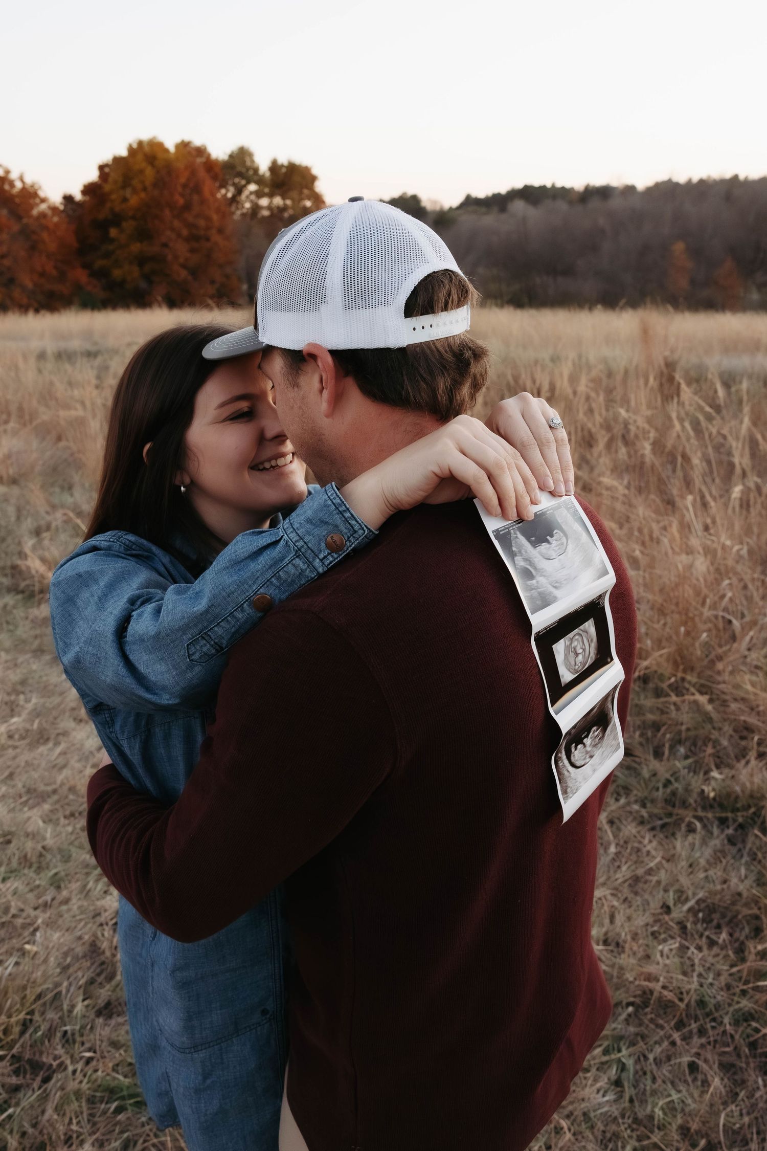 Couple sharing emotional moment while looking at ultrasound photos outdoors.