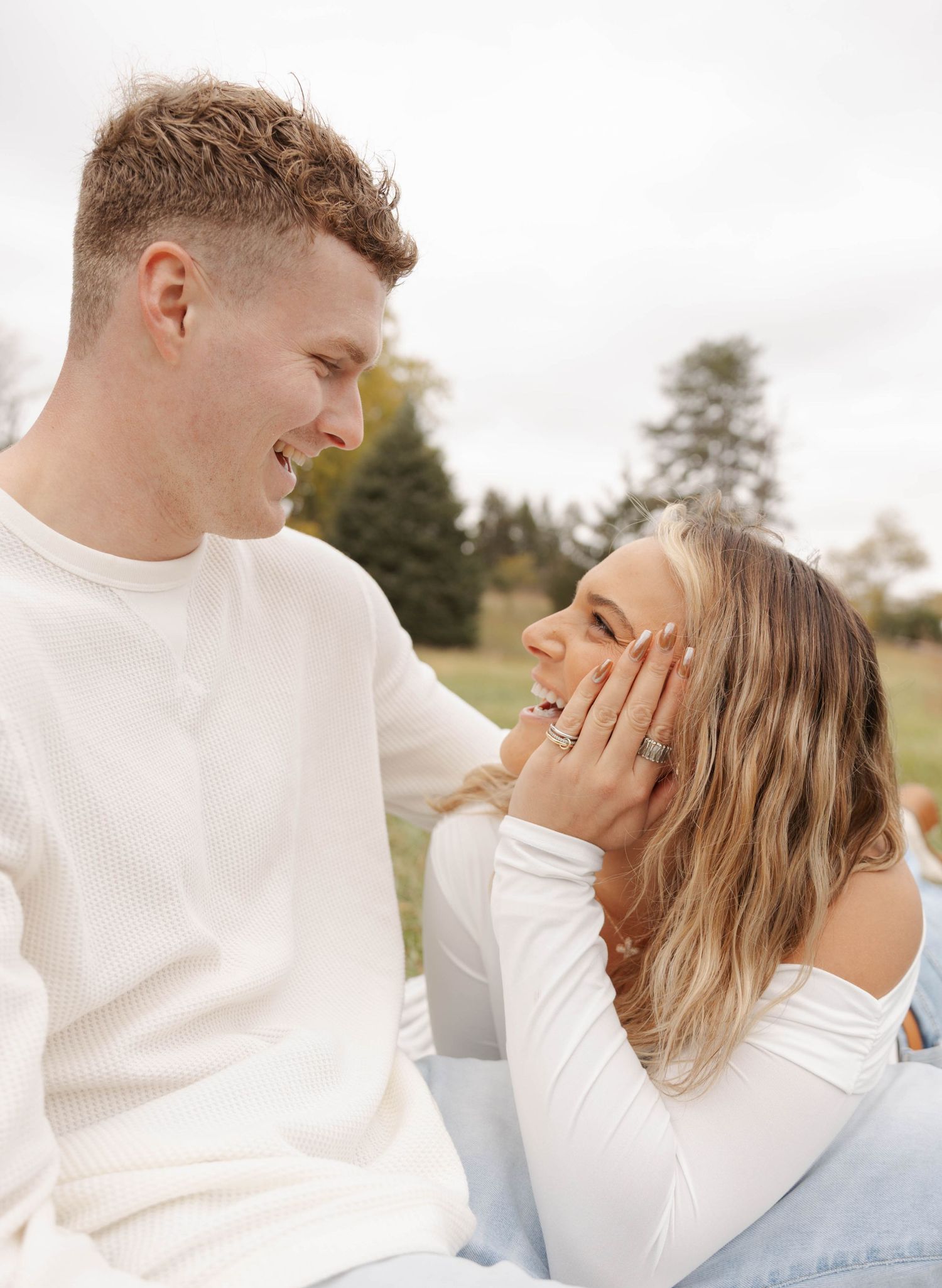 Intimate couple moment captured in white sweaters against outdoor backdrop.