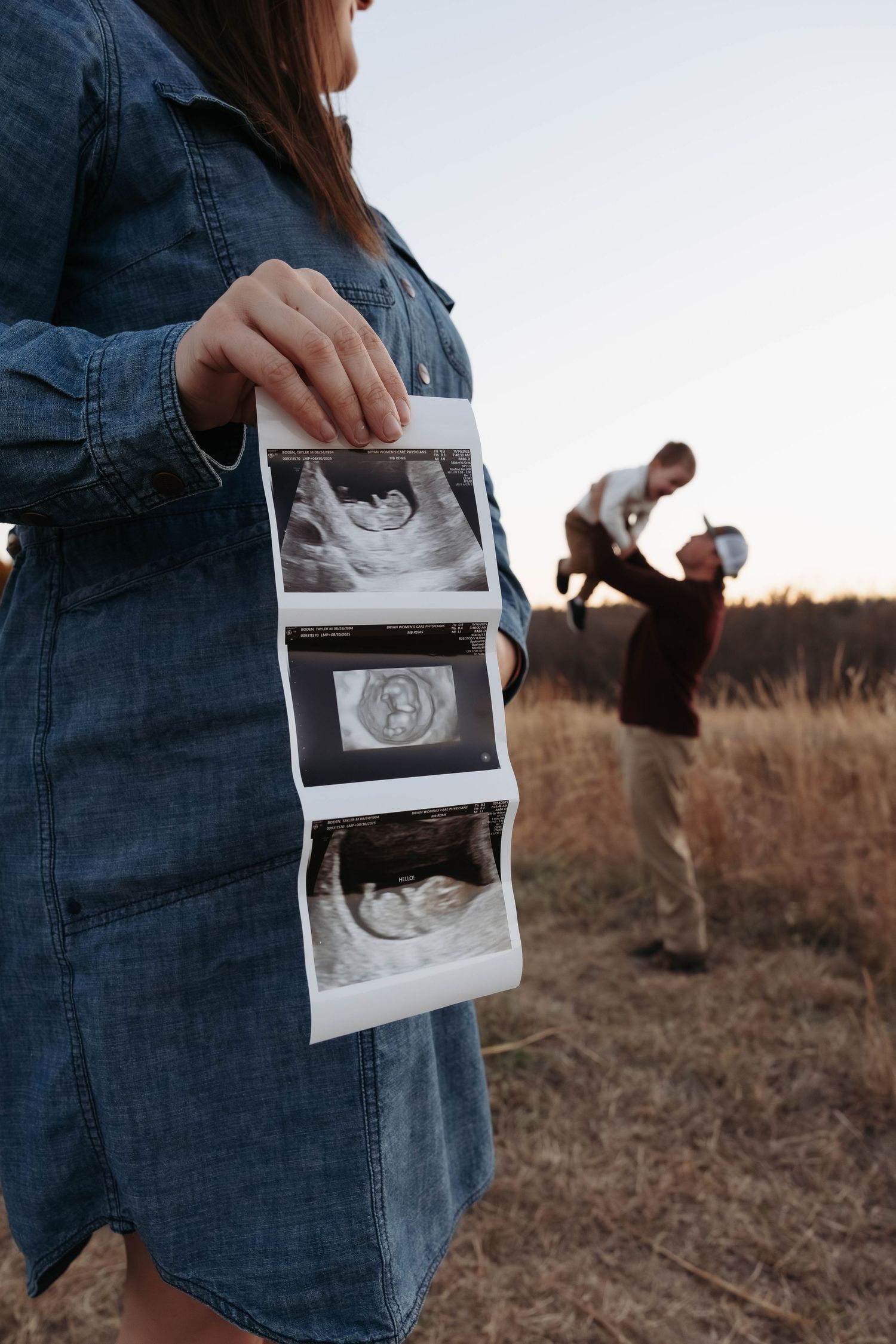 Person holding ultrasound photos while others play in autumn field at sunset.