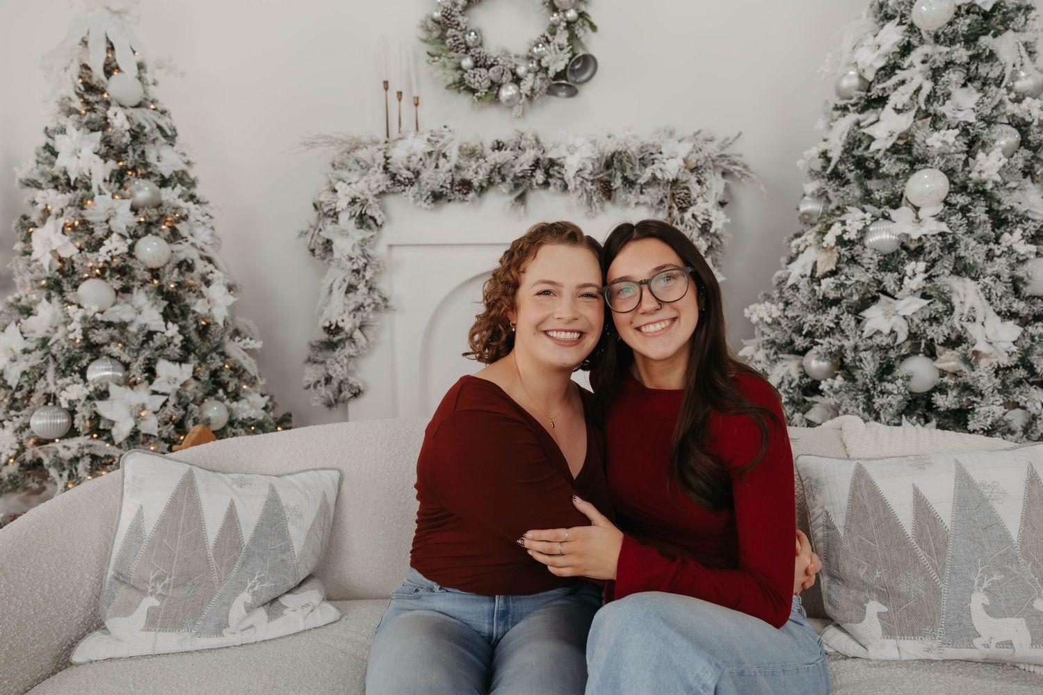 Two people embrace in cozy winter scene with flocked trees and holiday decorations.