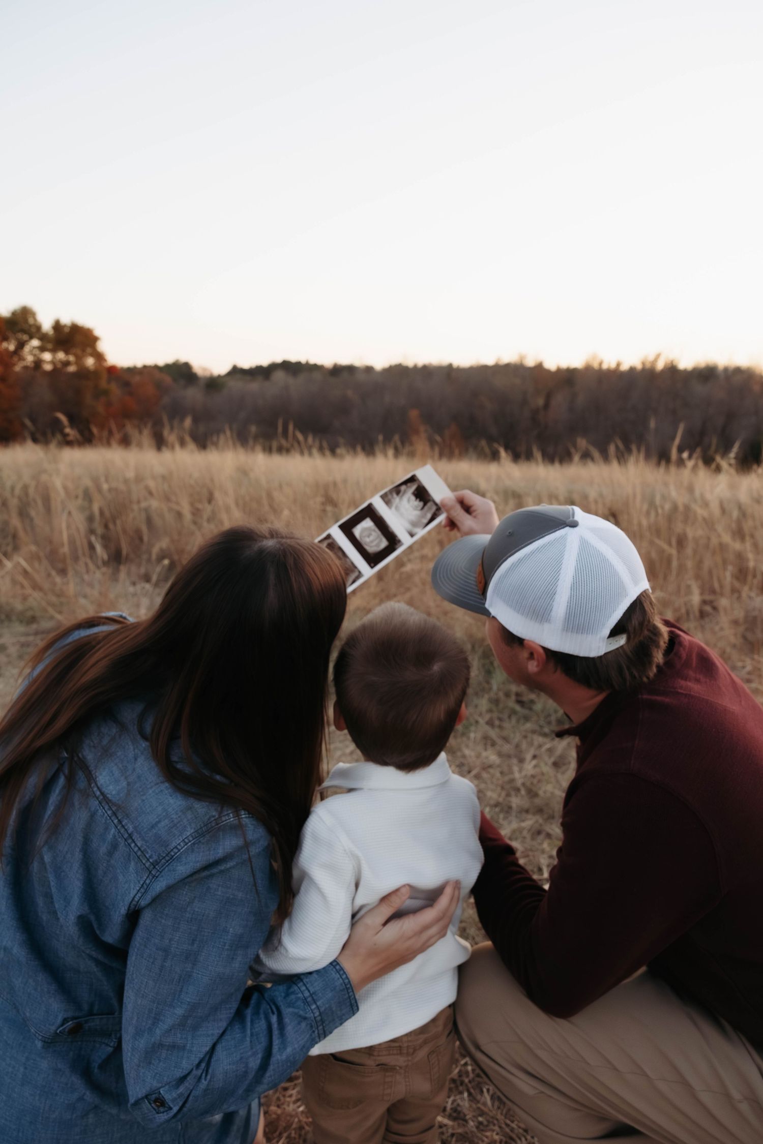 Group looking at photos together while sitting in a grassy field during sunset.