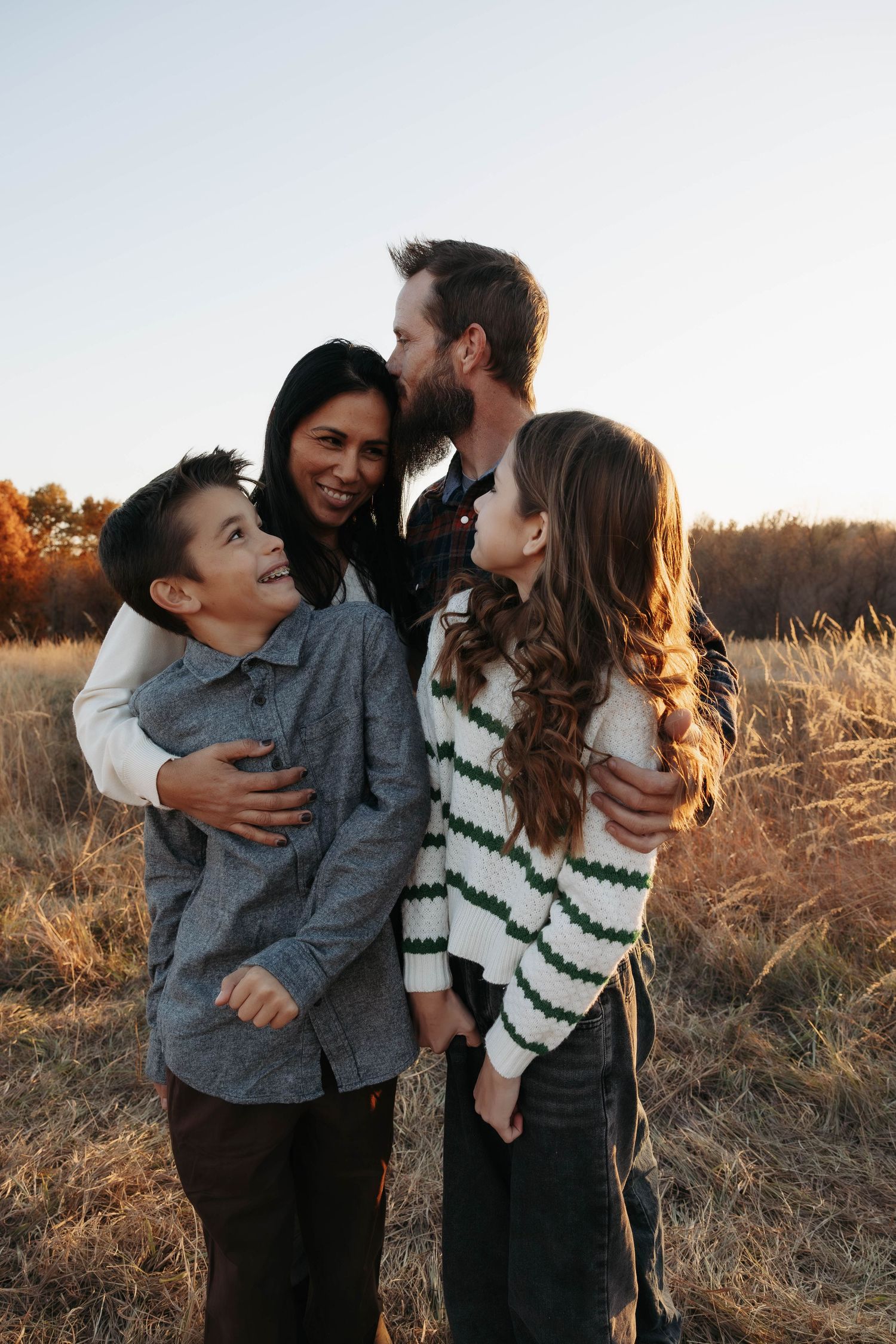 Family sharing warm embraces in a golden field during sunset.