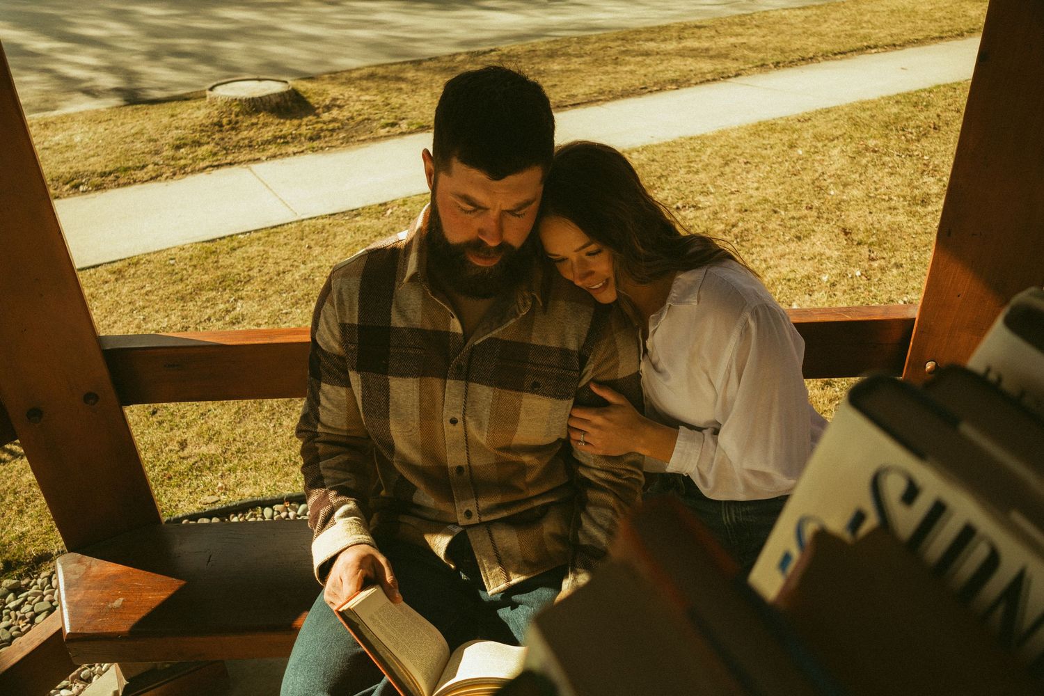 A couple shares an intimate moment while sitting together on a wooden bench in warm sunset lighting.