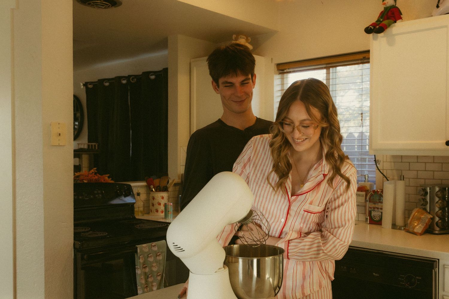 Two people in a kitchen preparing food with a stand mixer, captured in a warm vintage-style photograph.
