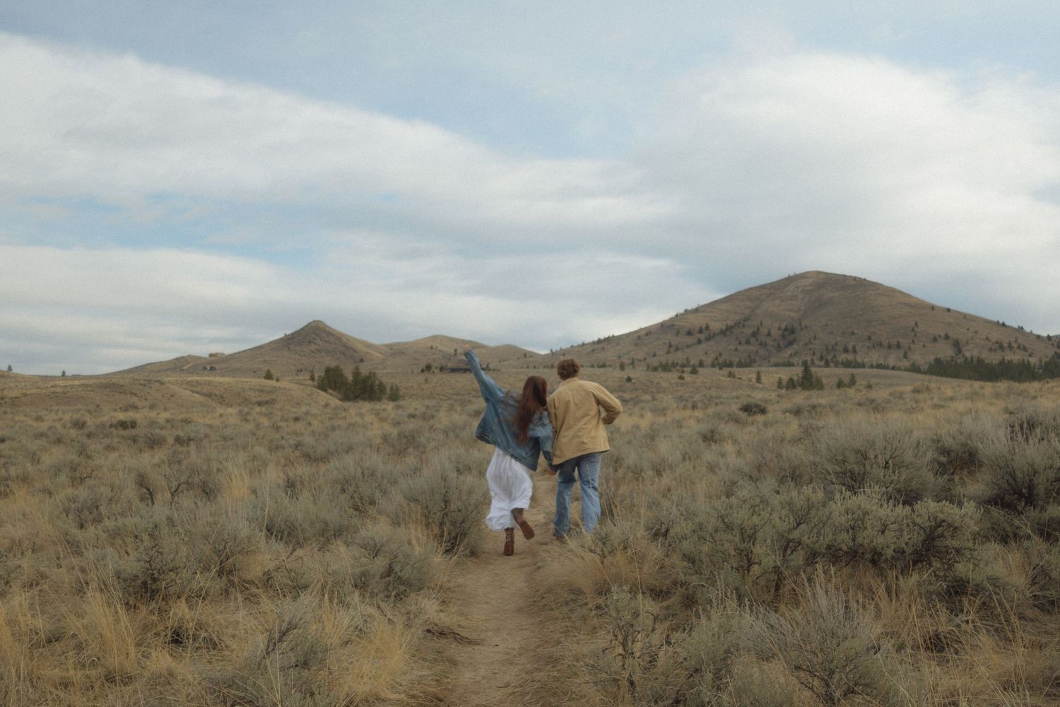 People explore a desert landscape with sagebrush and distant mountains under cloudy skies.