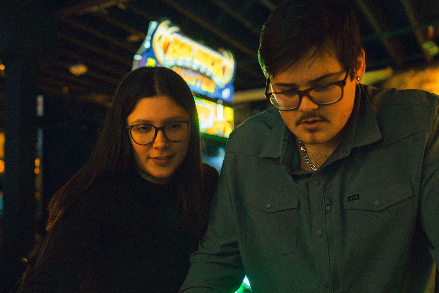 A person in glasses sits in dim lighting with neon signs visible in the background.
