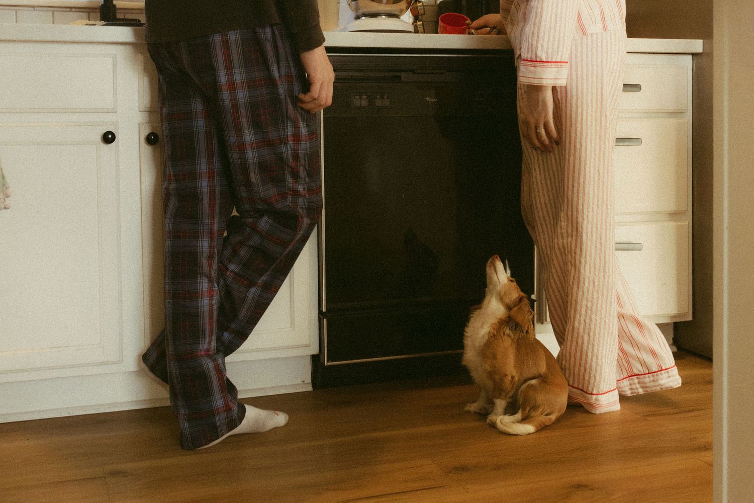 A person wearing plaid pajama pants and slippers stands in a cozy home interior with hardwood floors.