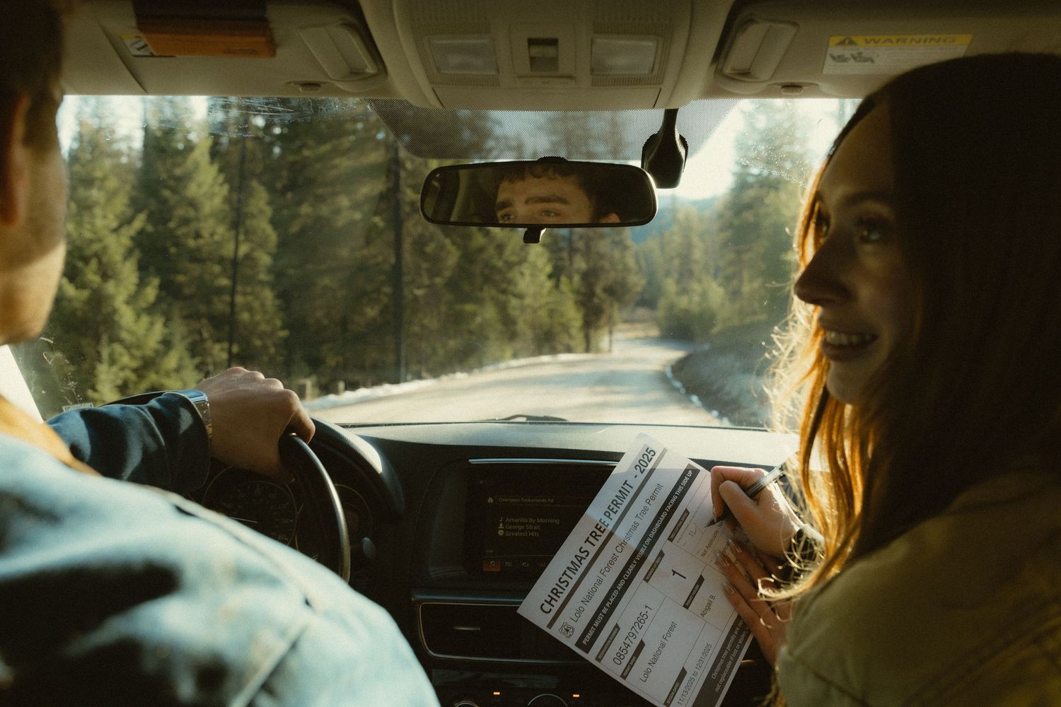 A person drives a car through a wooded area while holding papers, seen from multiple interior angles.
