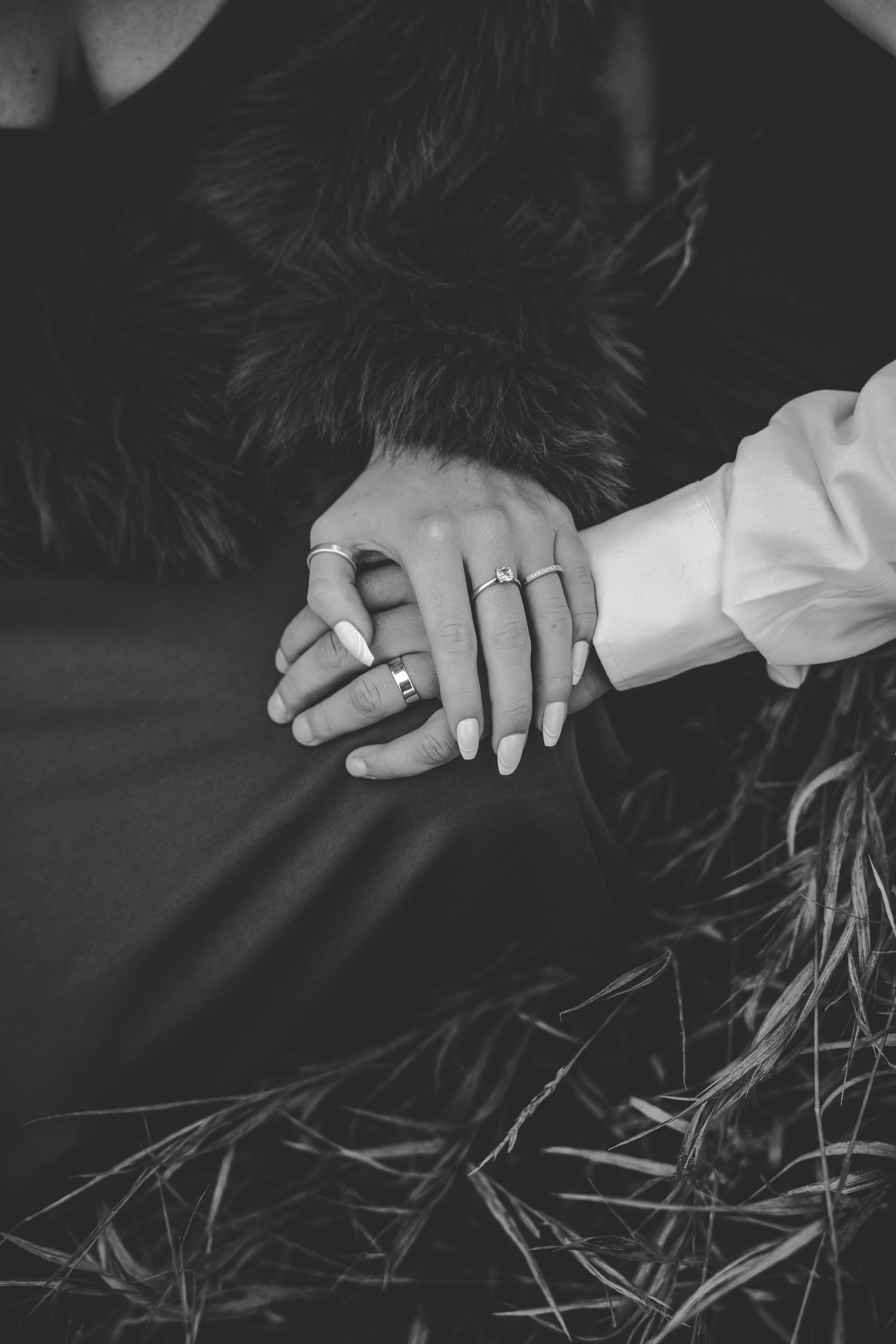 Close-up of hands with engagement ring resting on dark fabric.
