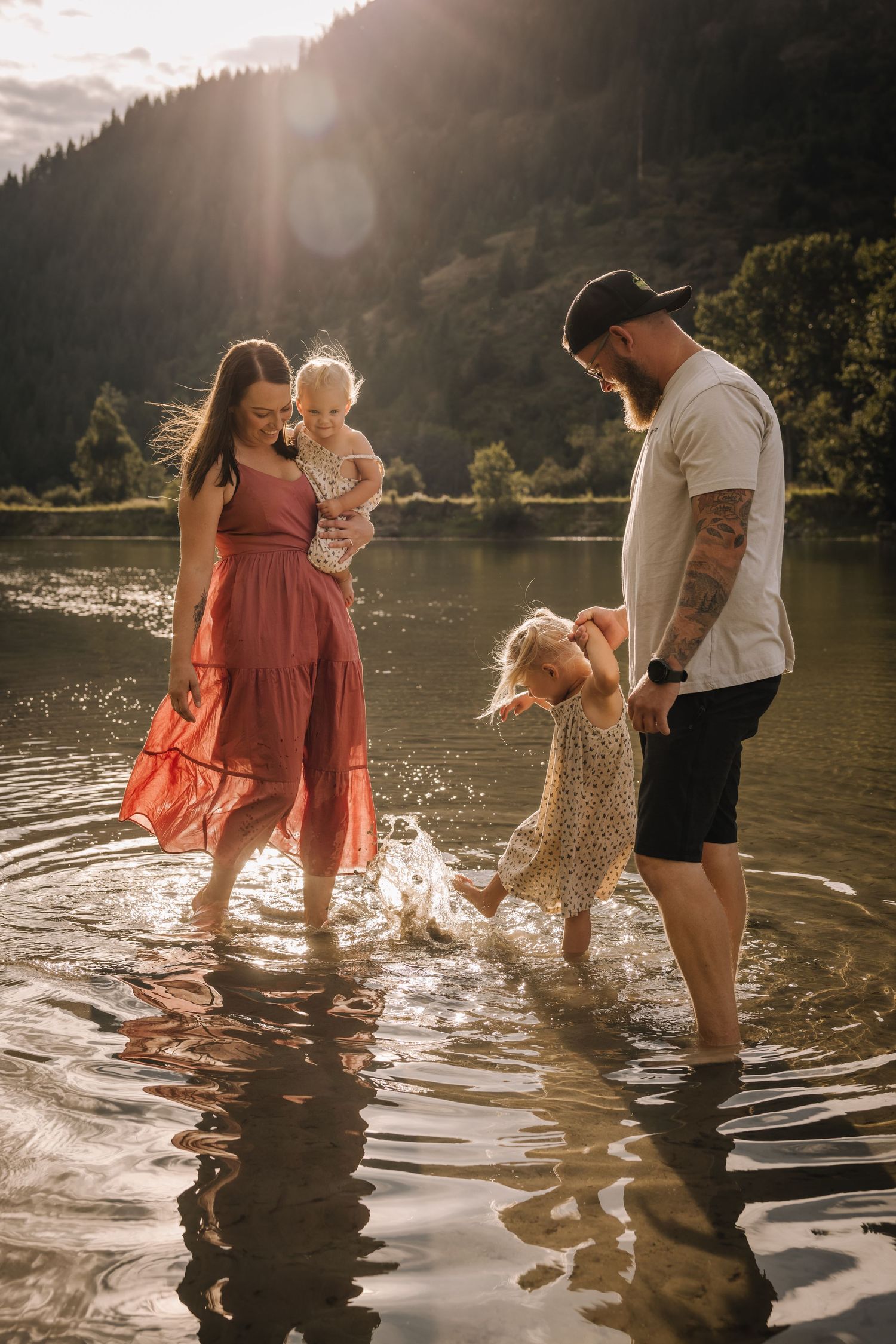 Family enjoying summer day together wading in lake water with sun flare.