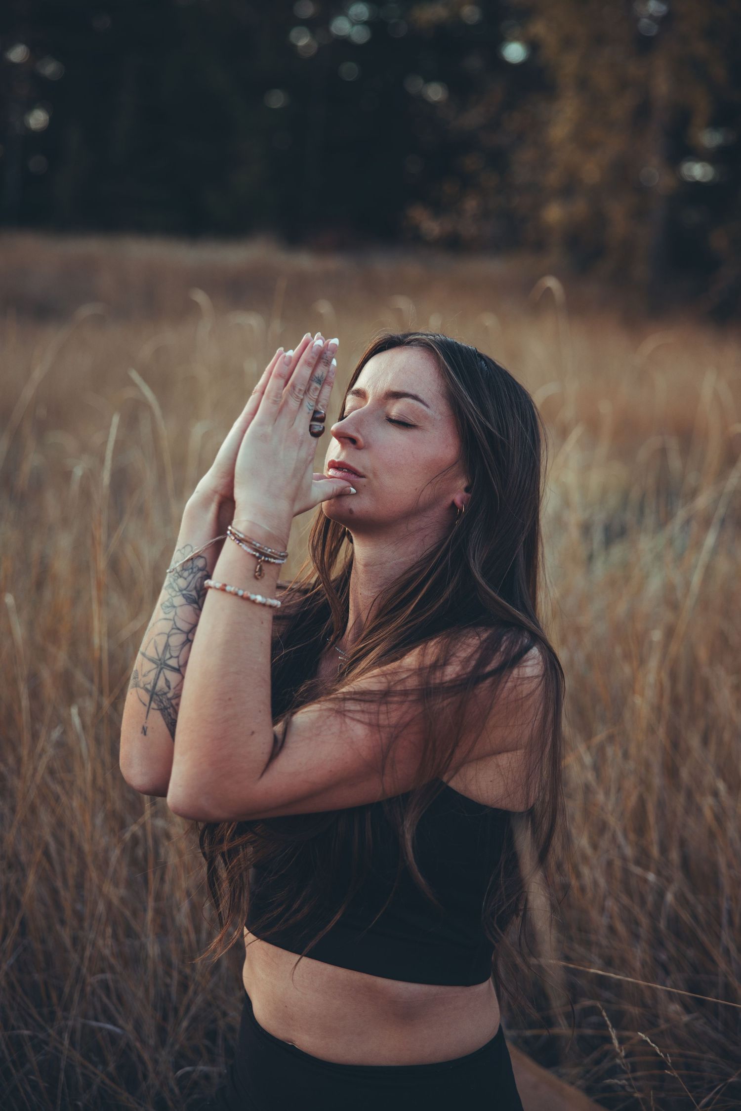 A person with tattoos poses expressively in a field of tall grass at golden hour.