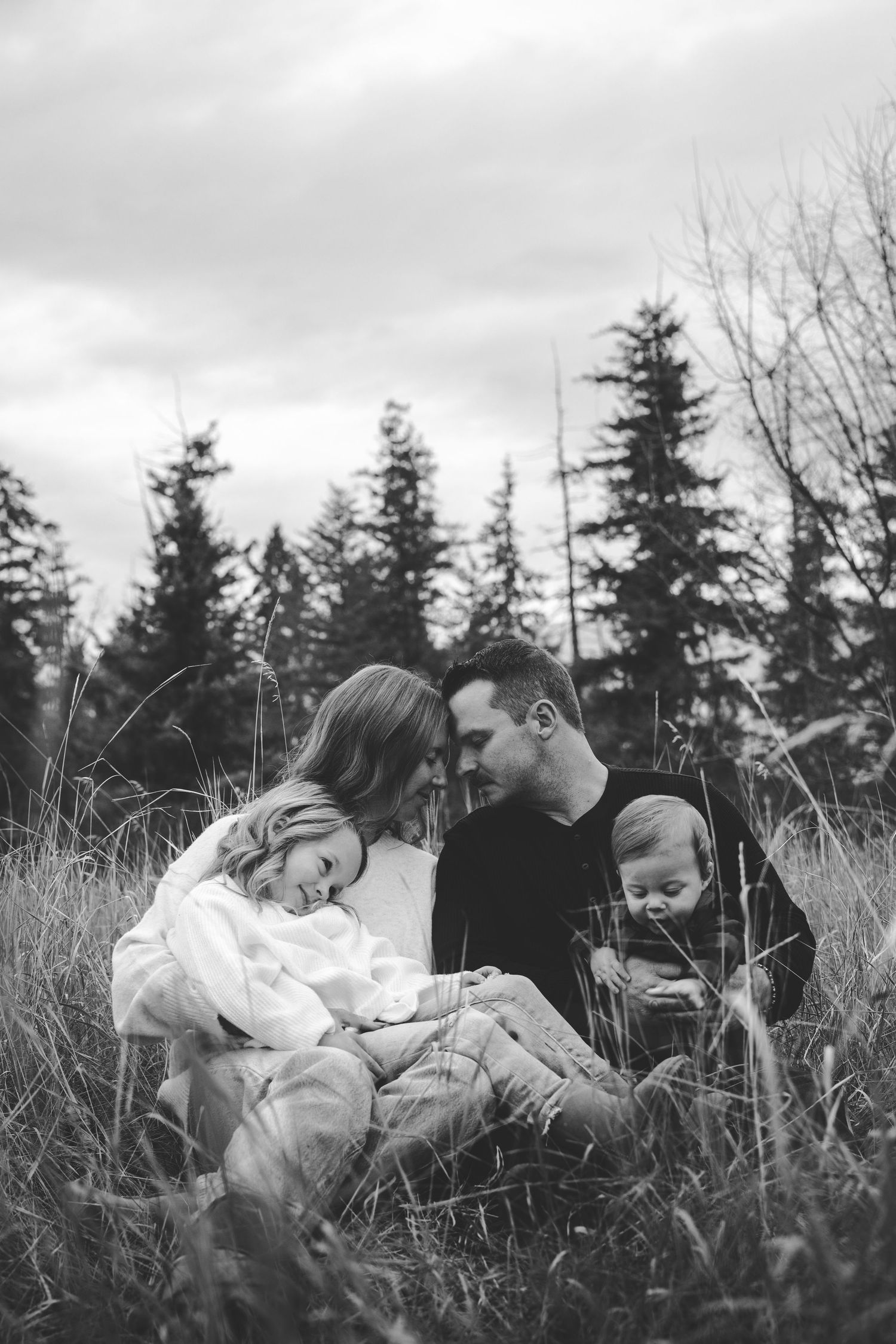 Family sharing tender moments while lying in tall grass on an overcast day.