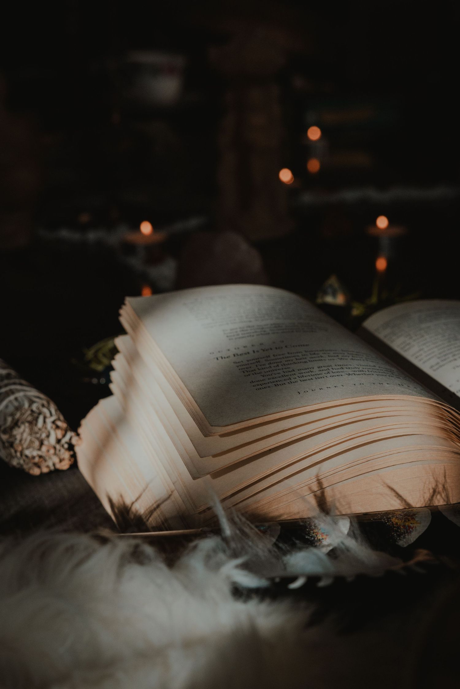 Open book with pages fanned out in moody lighting with candles glowing in the background.