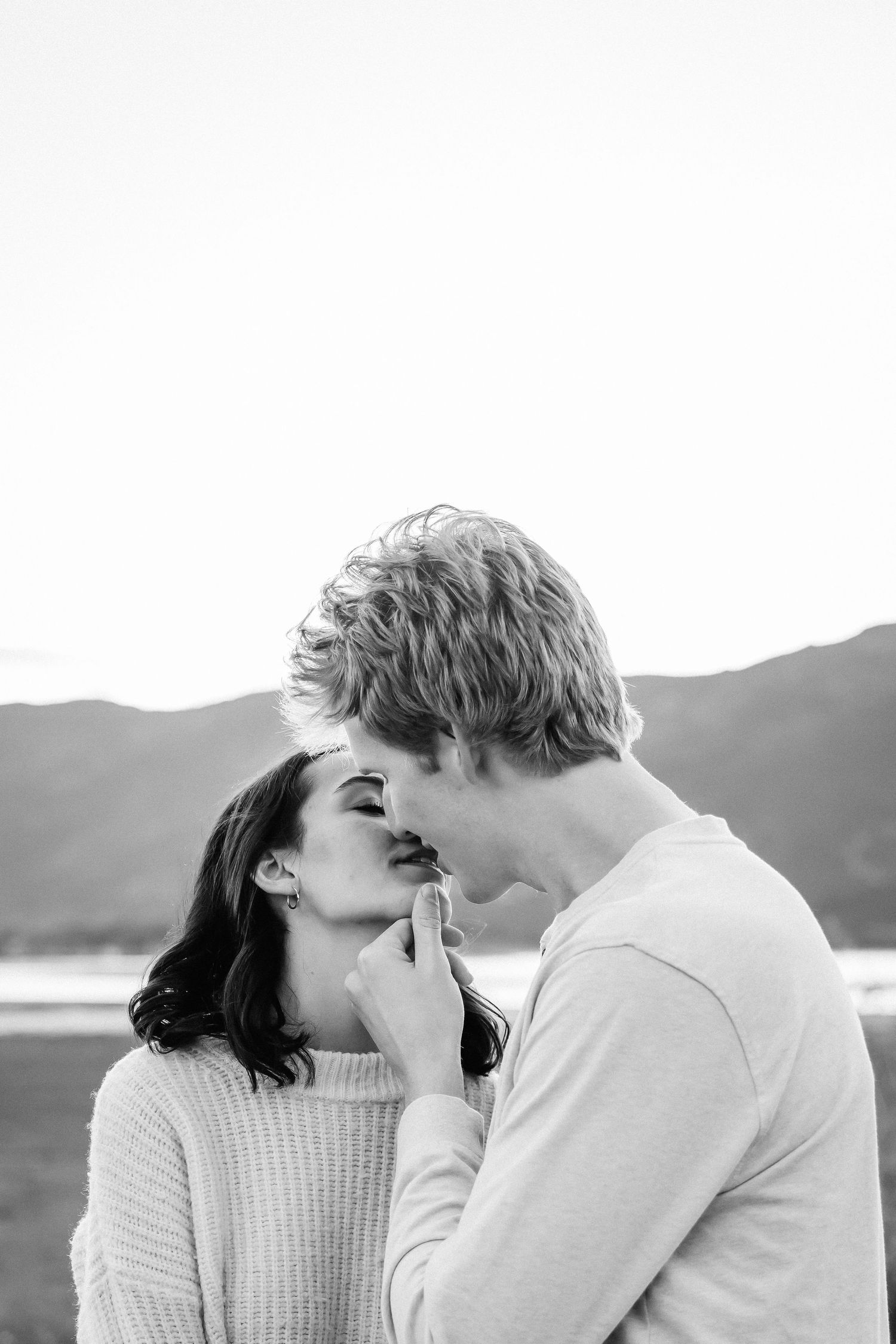 Romantic couple sharing intimate moments in black and white photography against a mountain backdrop.