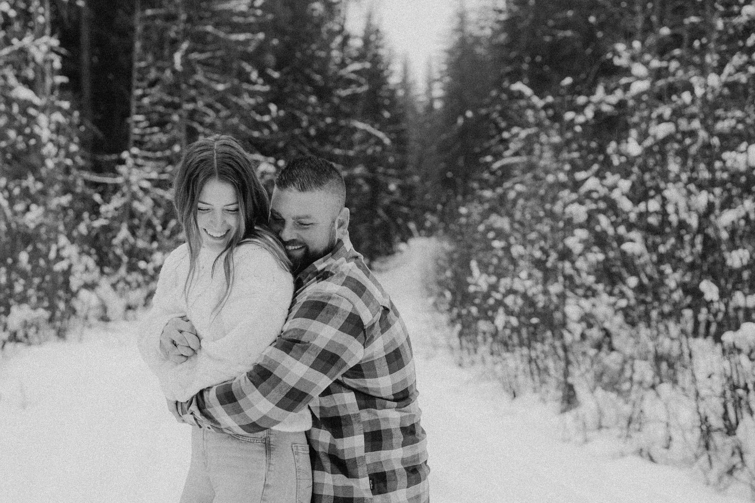 Winter engagement photos in snowy forest with couple in plaid flannel.