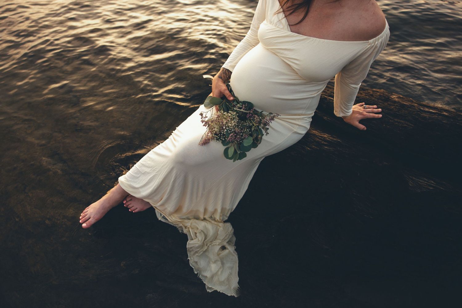 Woman in flowing white dress dancing by water at sunset.
