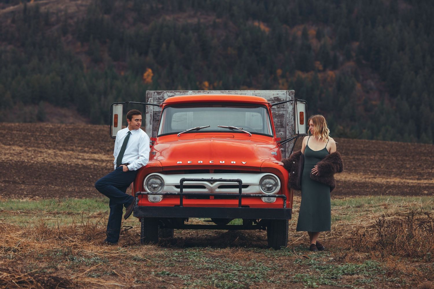 Classic red pickup truck parked in autumn field with mountains in background.