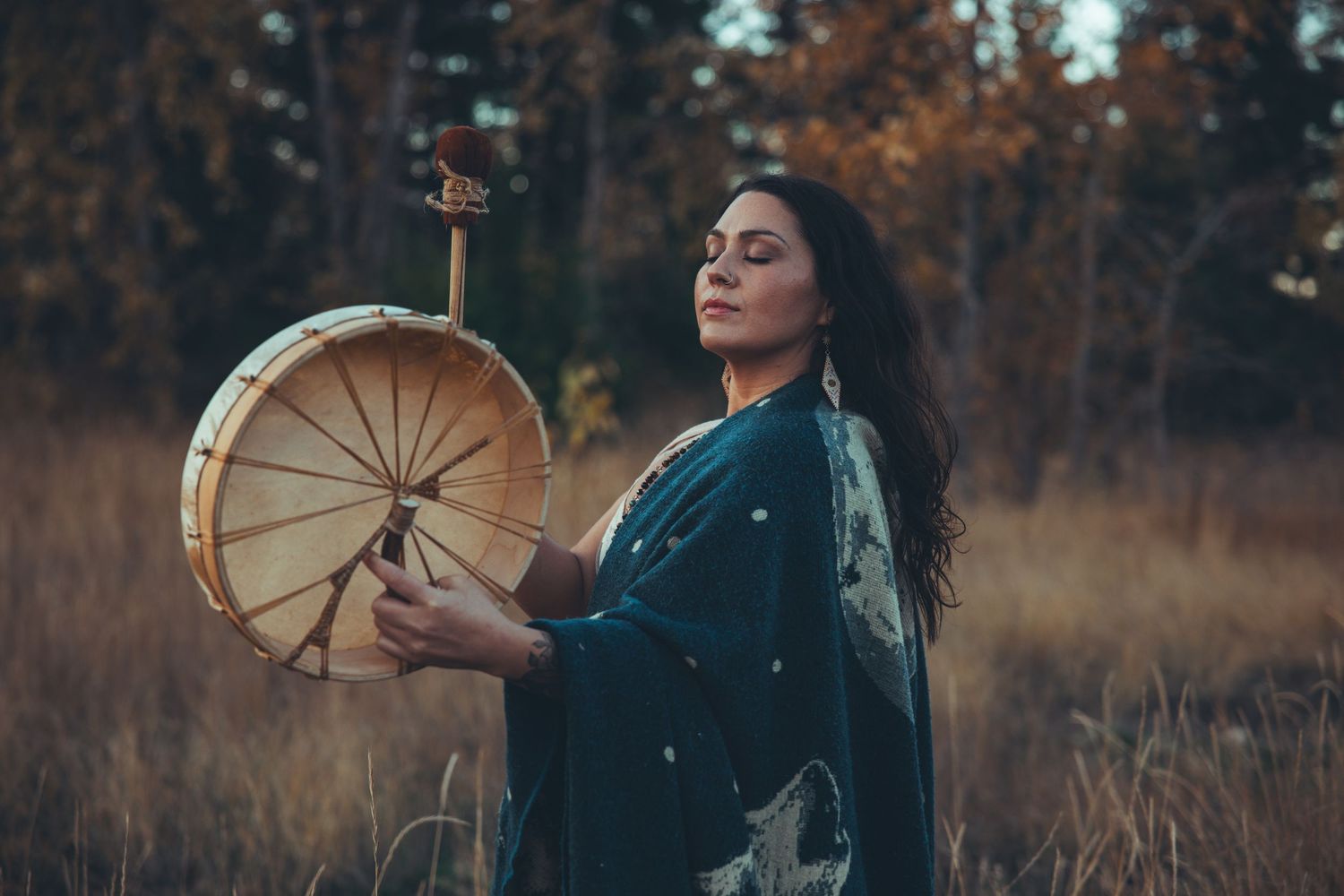 Person holding a traditional drum in an autumn field during golden hour.