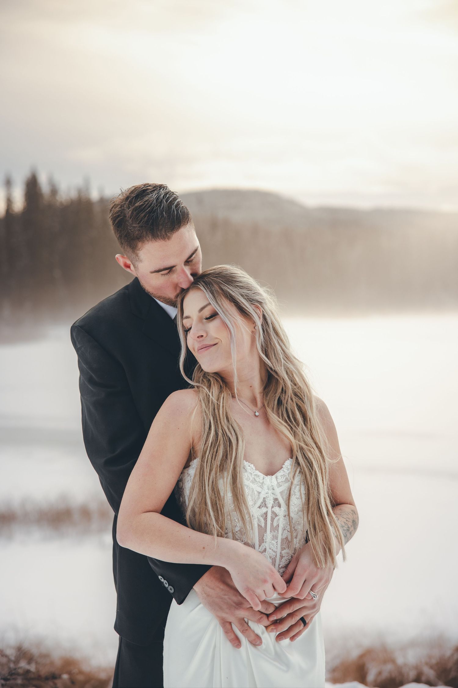 Romantic winter wedding photos of couple embracing in snowy landscape at sunset.