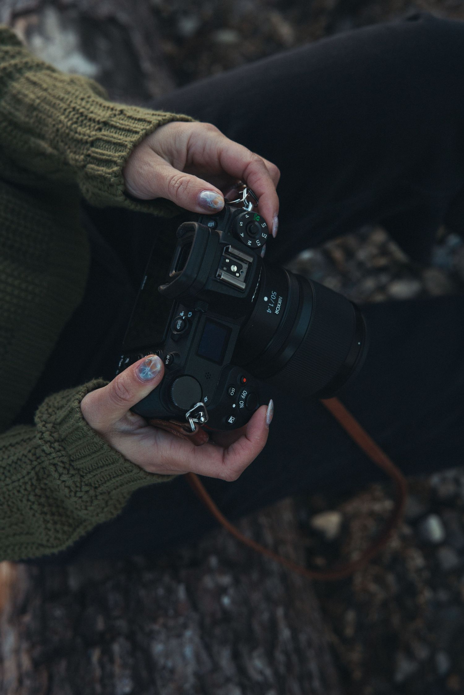 Hands holding a black camera against dark background.