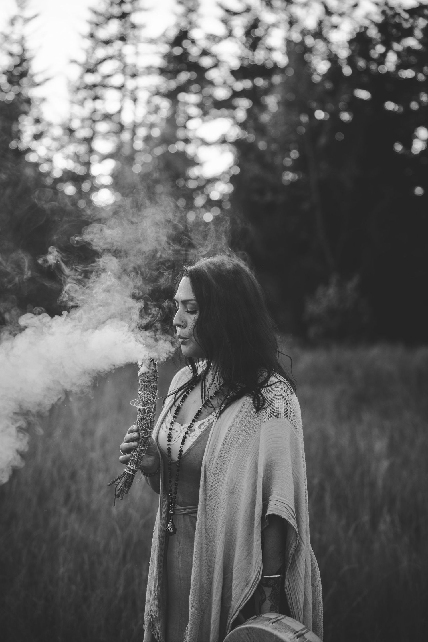 Person exhaling smoke in a moody outdoor setting with trees in the background.
