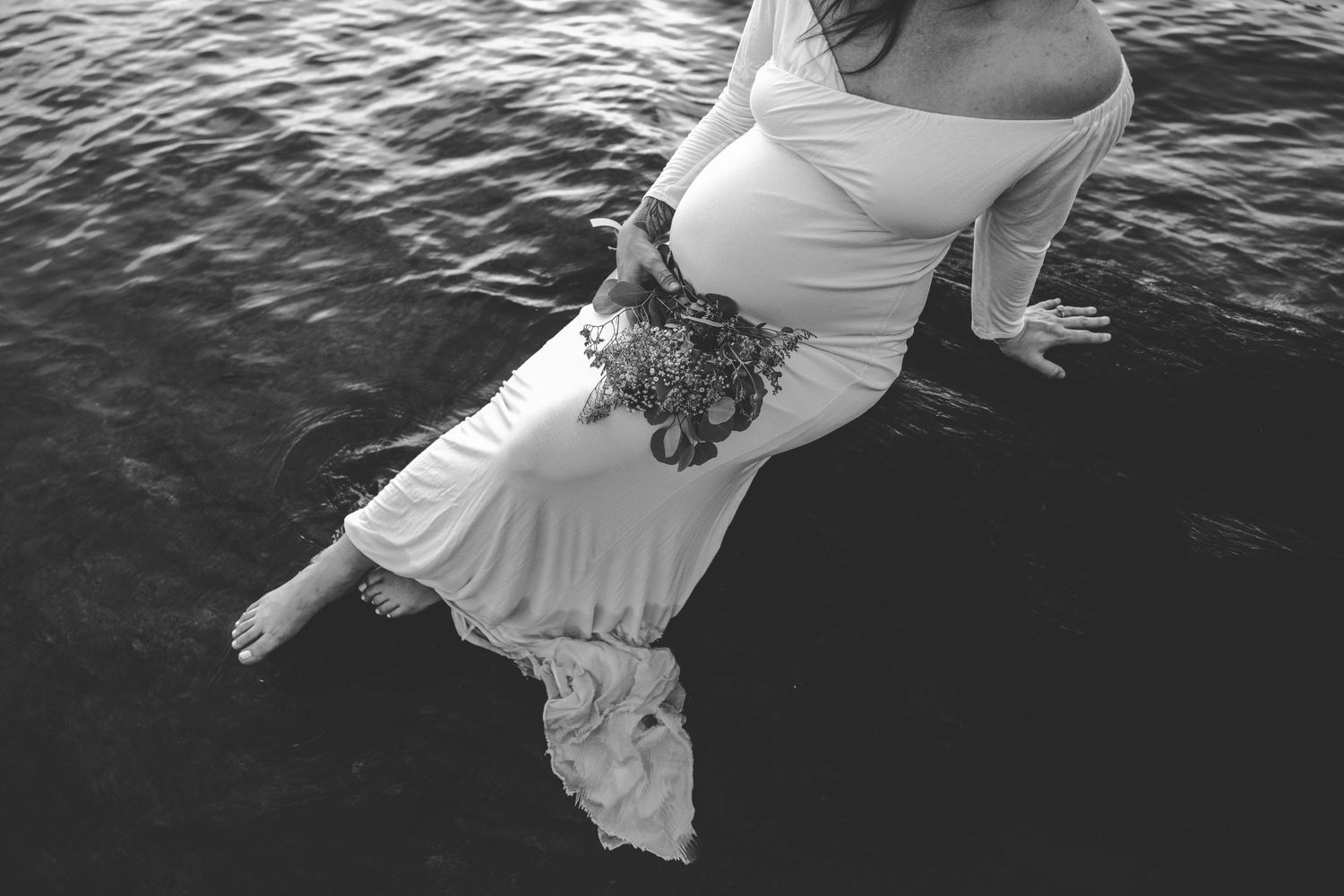 Woman in white dress floating in dark water with flowers on her waist.