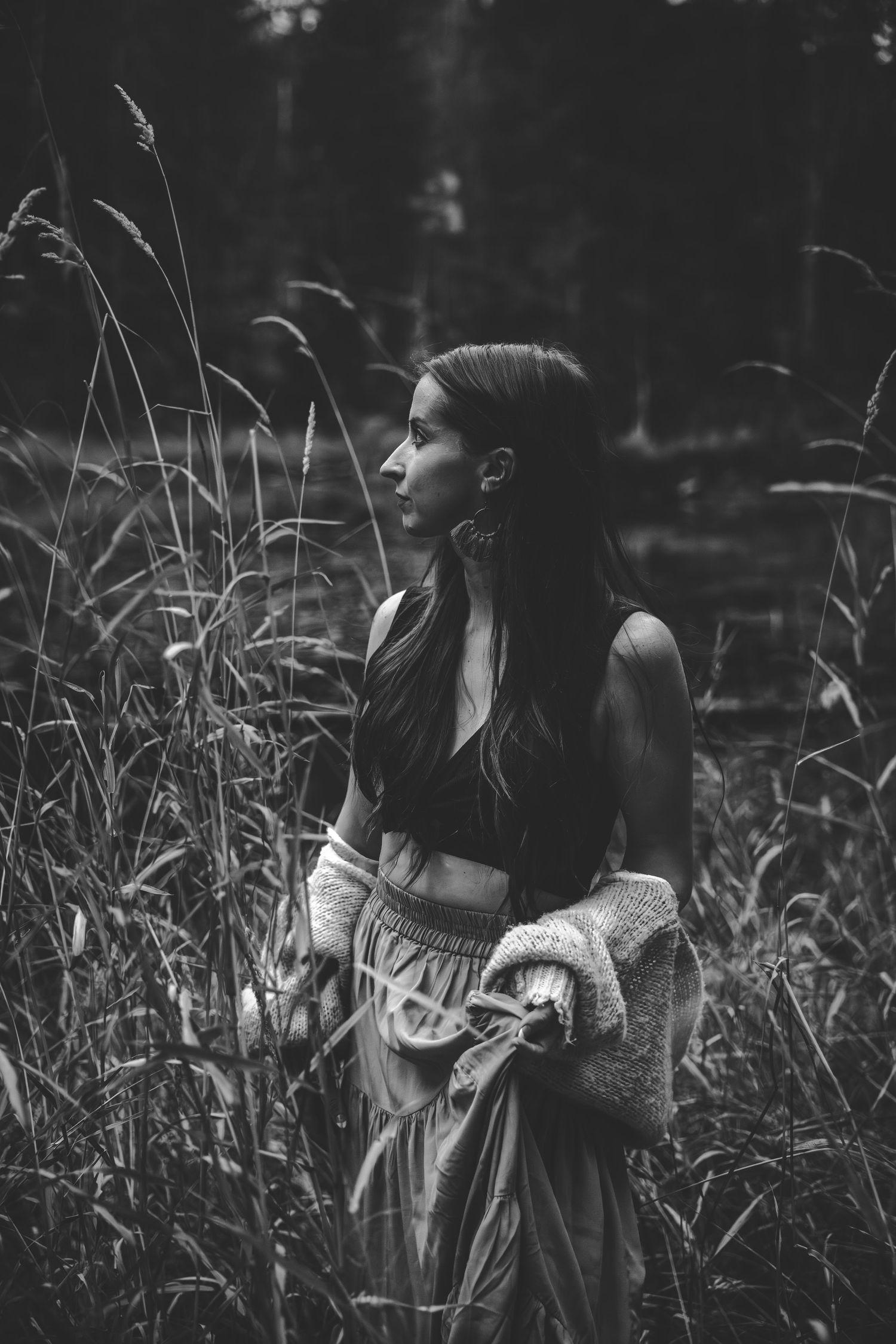 Artistic black and white photo of a figure standing among tall grass in a moody natural setting.
